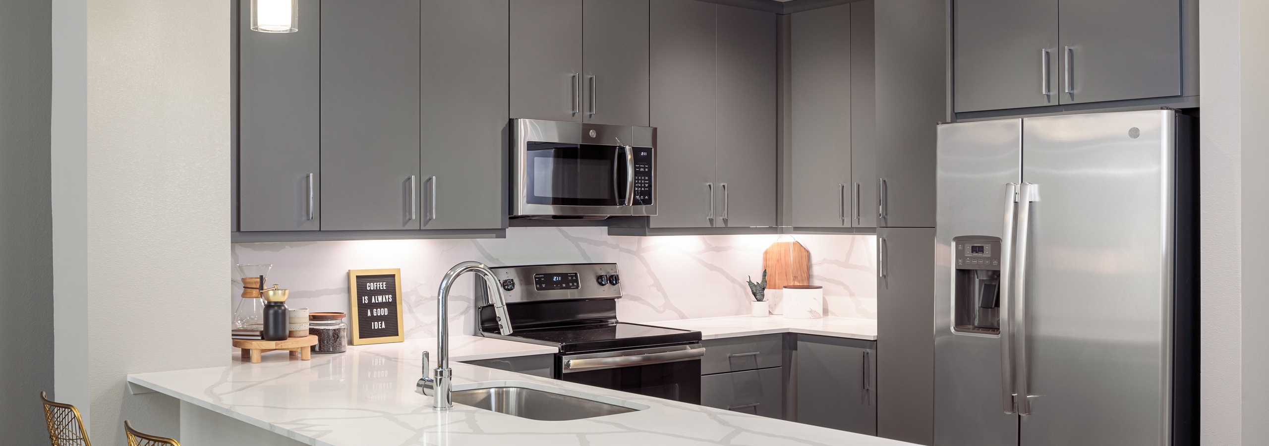 AMLI Addison kitchen with grey wood cabinets and white countertops with matching backsplash and stainless steel appliances