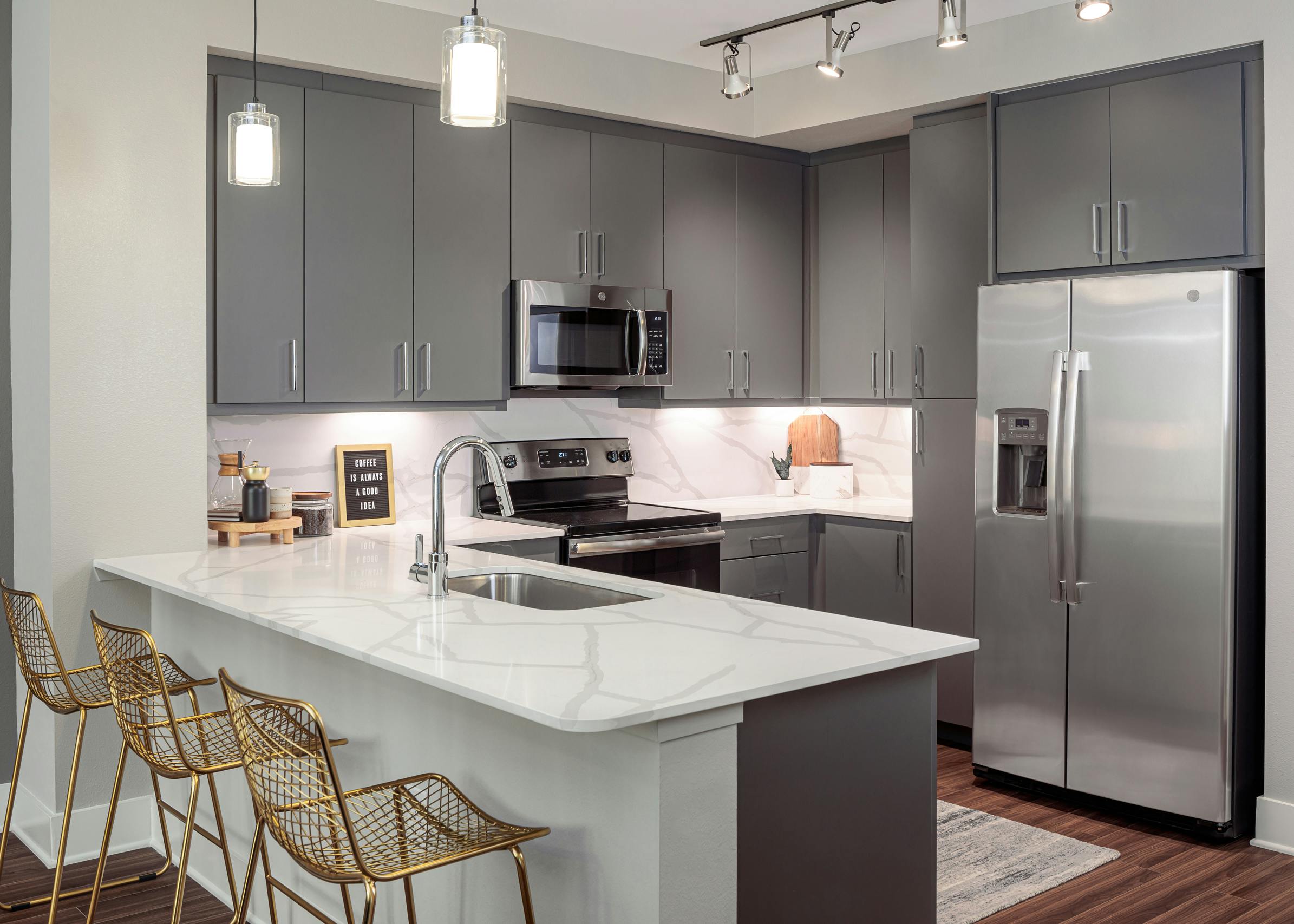AMLI Addison kitchen with white island and quartz countertops with three barstools and a built in desk next to refrigerator