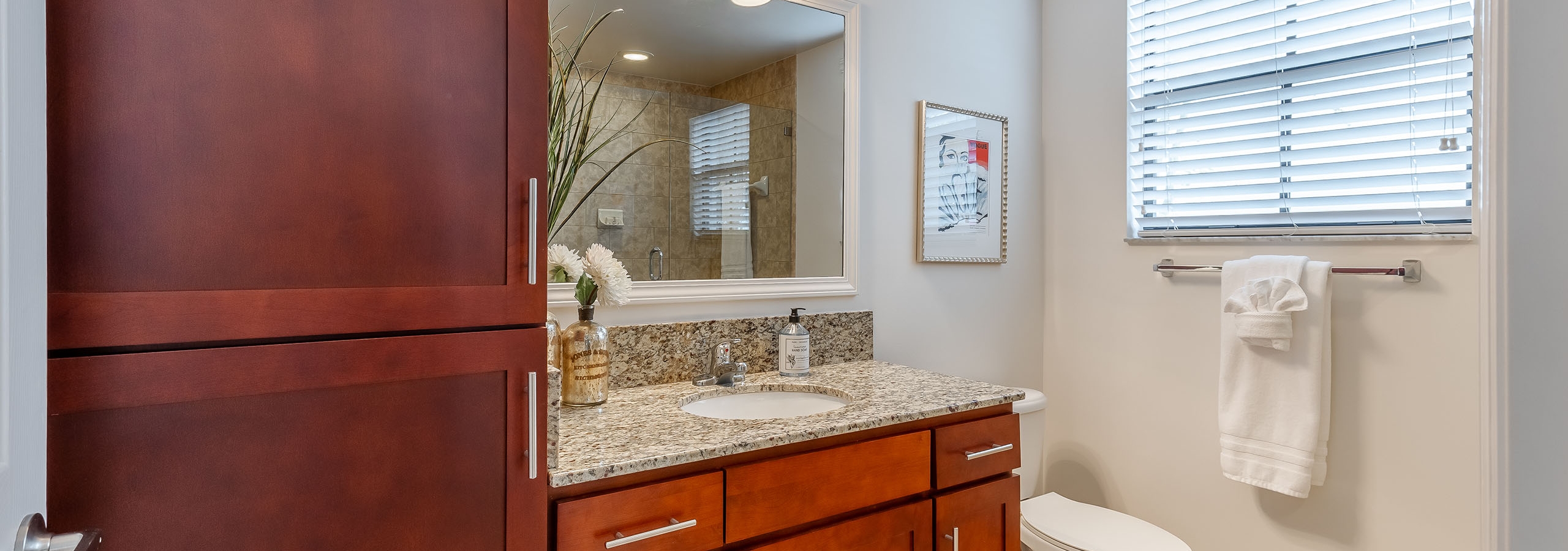 Interior view of AMLI Toscana Place apartment bathroom with wood vanity and granite counter with mirror above and side window