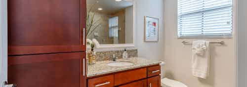 Interior view of AMLI Toscana Place apartment bathroom with wood vanity and granite counter with mirror above and side window