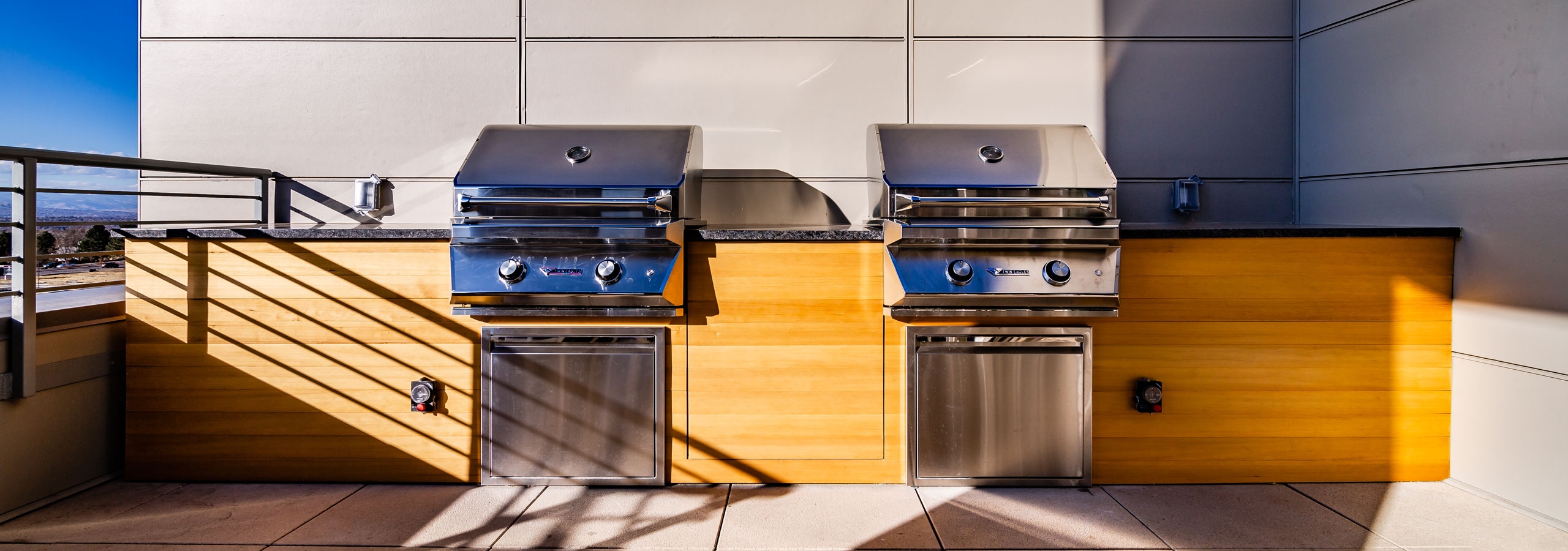 Daytime view of outdoor rooftop lounge with two stainless steel barbecue stations at AMLI Littleton Village apartments