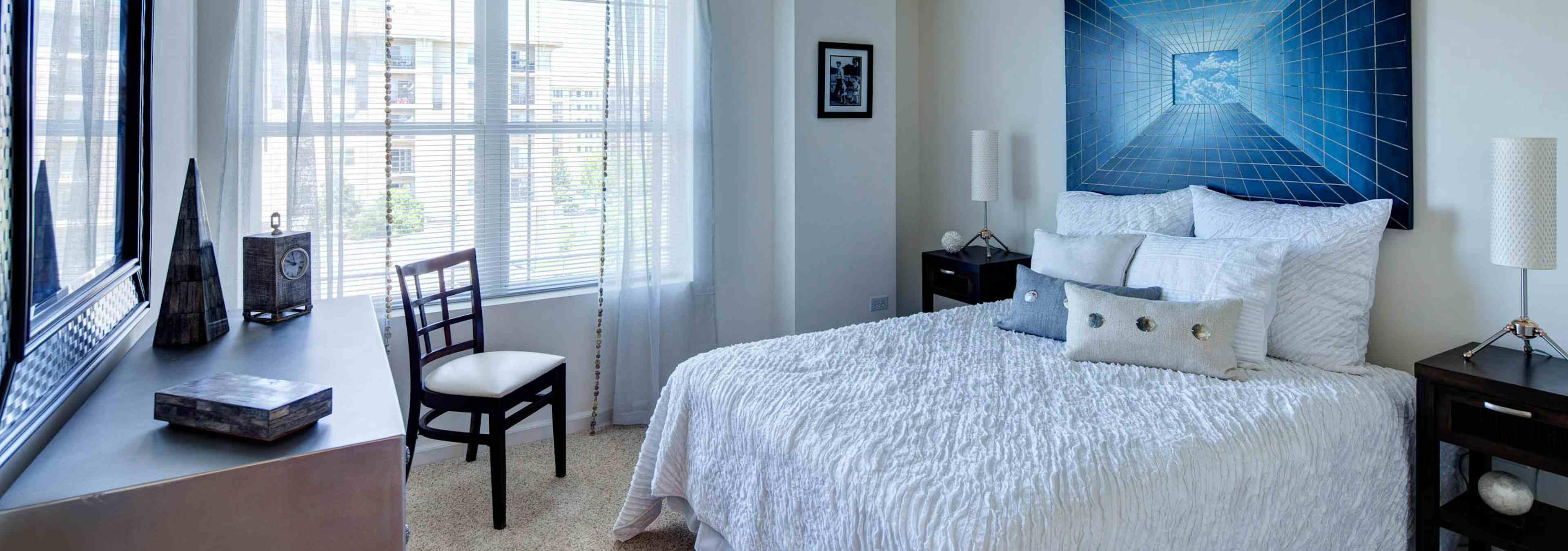 Bedroom at AMLI at Seven Bridges with a large window behind an elegant white bed with a large royal blue art piece above it