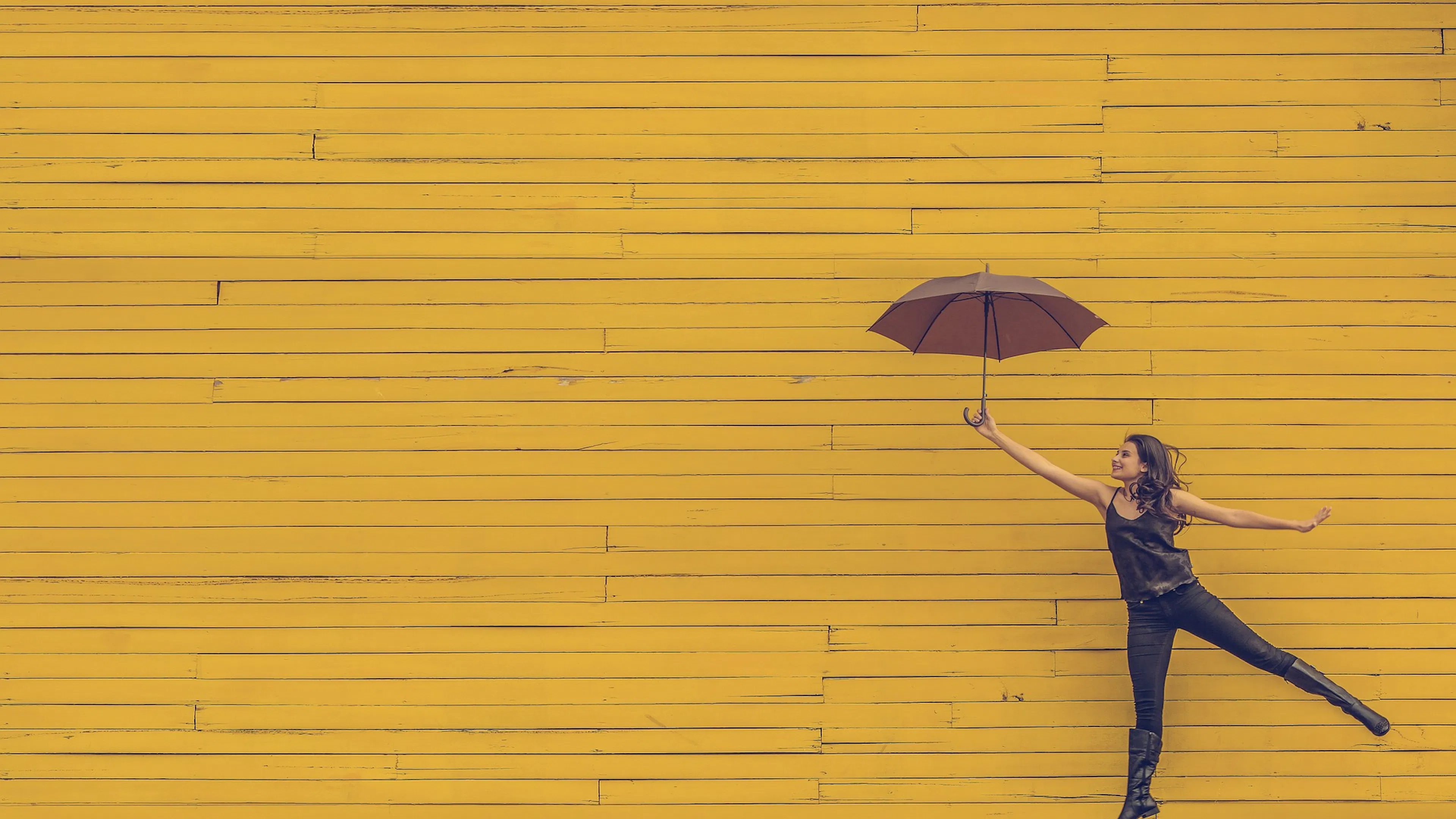 yellow wood wall with woman in black floating across with umbrella