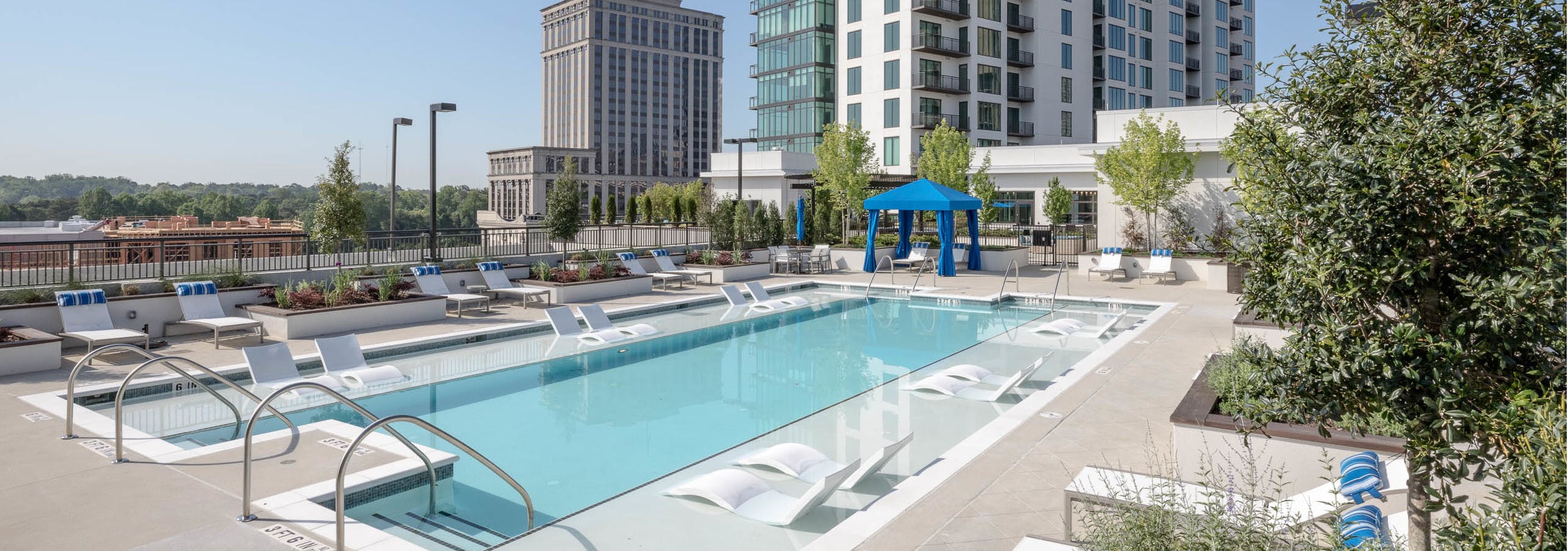 Daytime view of the pool at AMLI 3464 with surrounding white lounge chairs and a royal blue canopy in the background