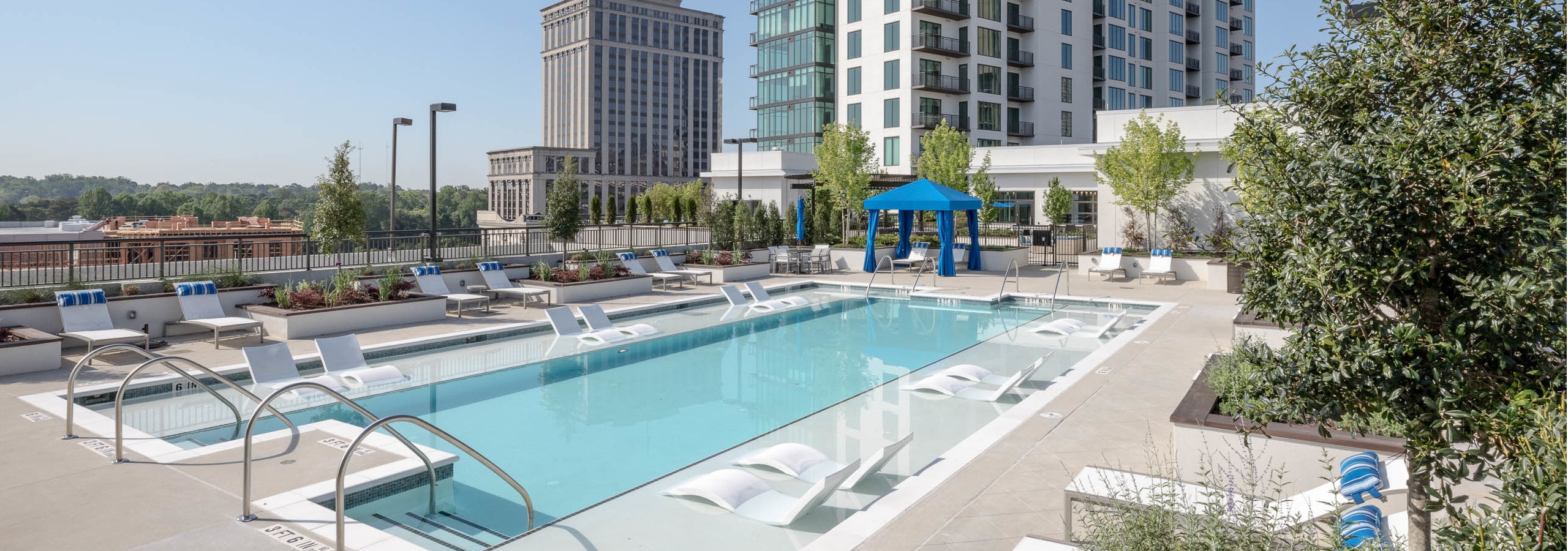 Daytime view of the pool at AMLI 3464 with surrounding white lounge chairs and a royal blue canopy in the background