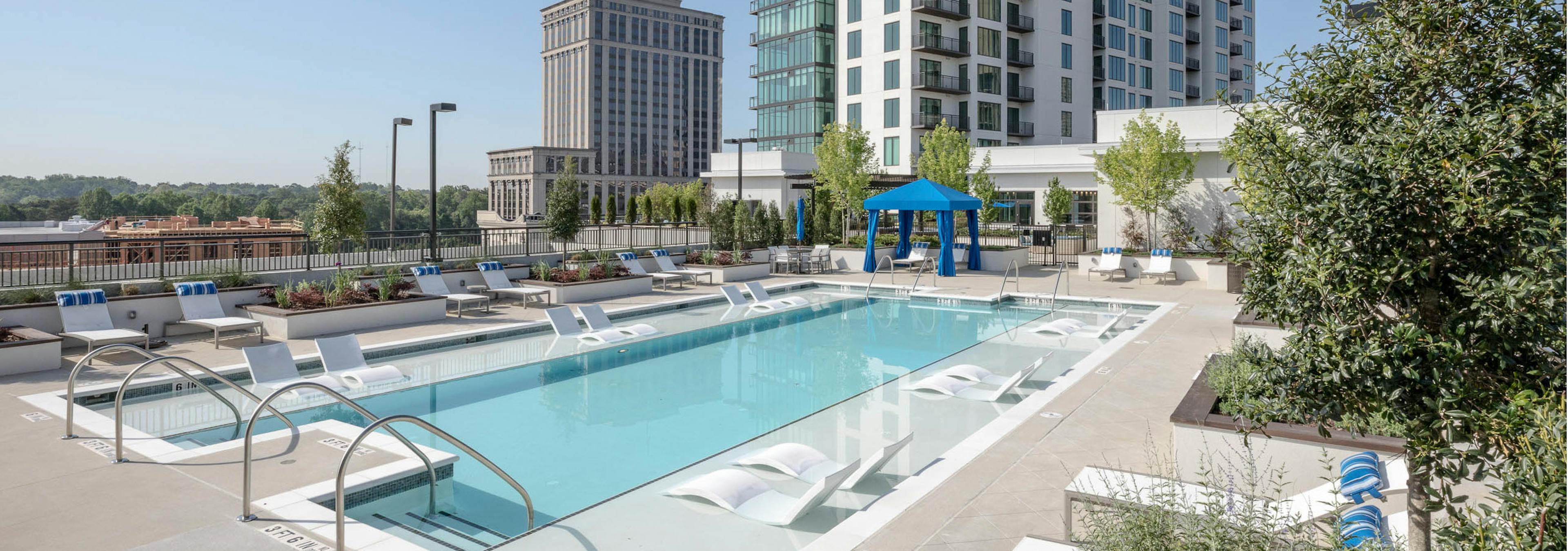 Daytime view of the pool at AMLI 3464 with surrounding white lounge chairs and a royal blue canopy in the background 