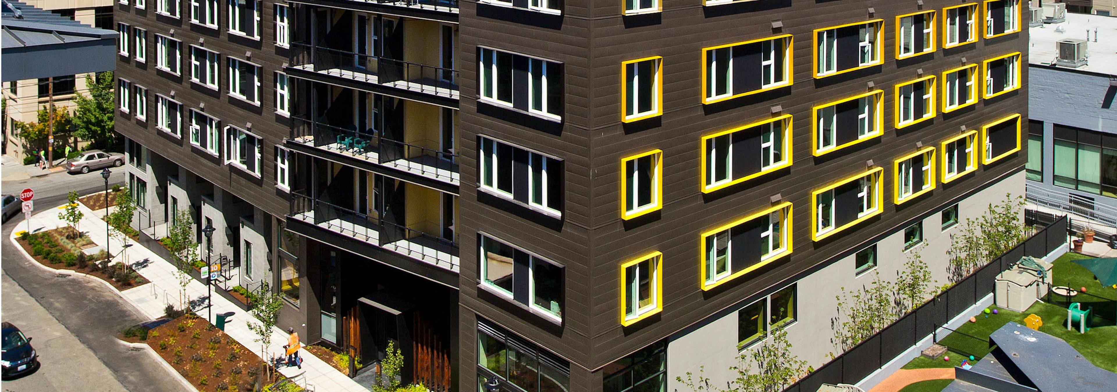 Exterior view of AMLI South Lake Union second building with brown walls and yellow highlights sidewalk with trees and outdoor bench 