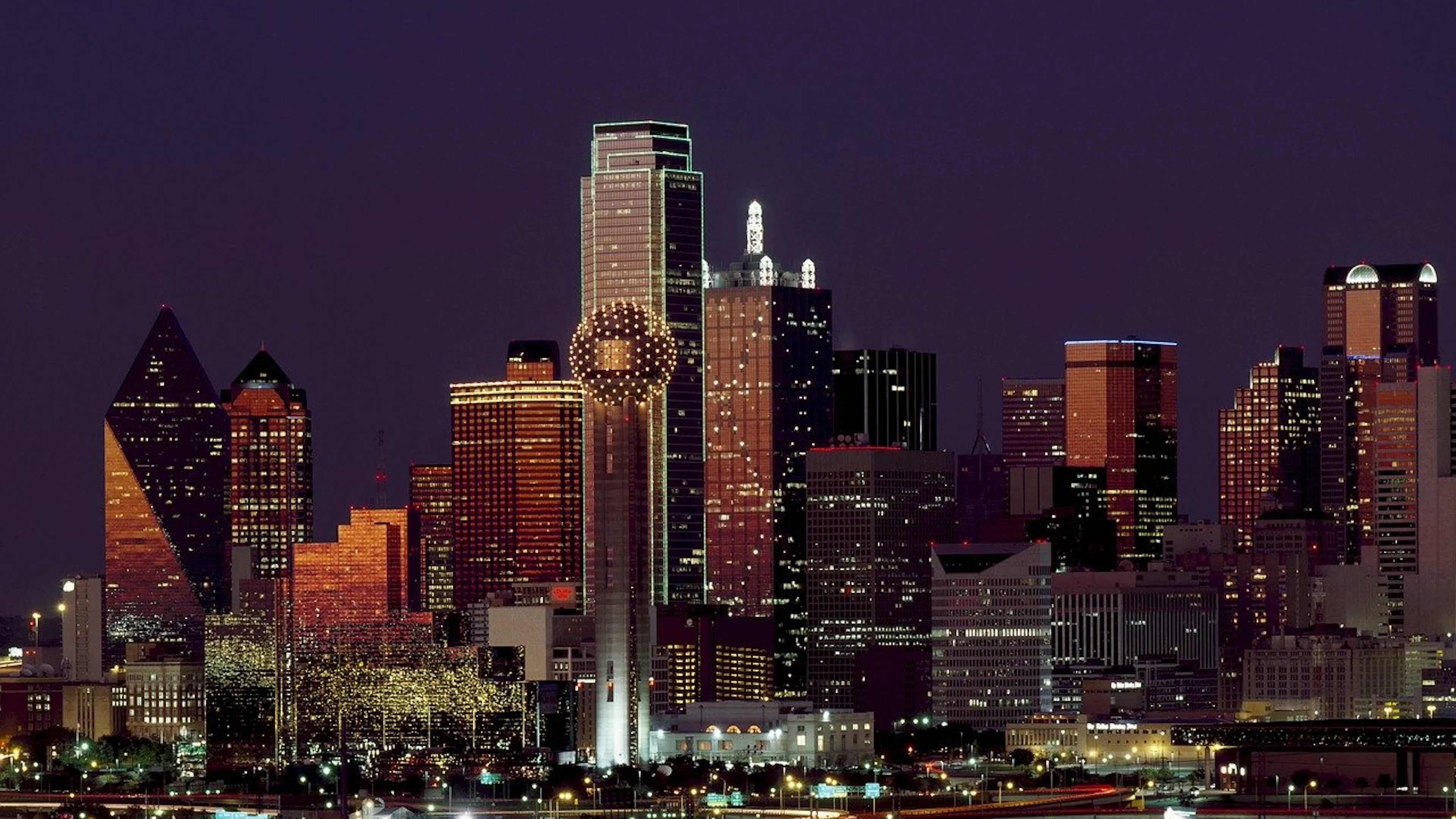 The Dallas skyline at night with the buildings and highways lit up against the dark sky