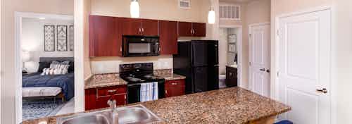 Interior view of a kitchen at AMLI Arista apartments with a view of a counter top and faucet and fridge and peek into bedroom