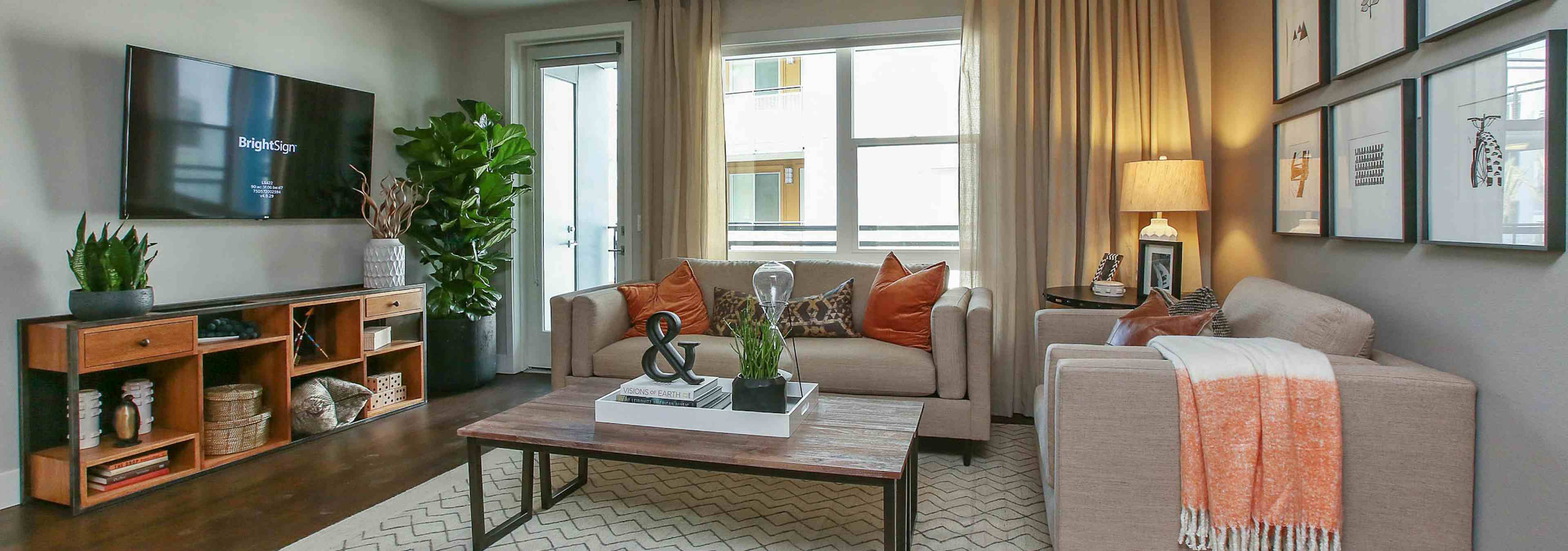 Interior view of AMLI Uptown Orange apartment living room with large couch and table and love seat in front of large windows