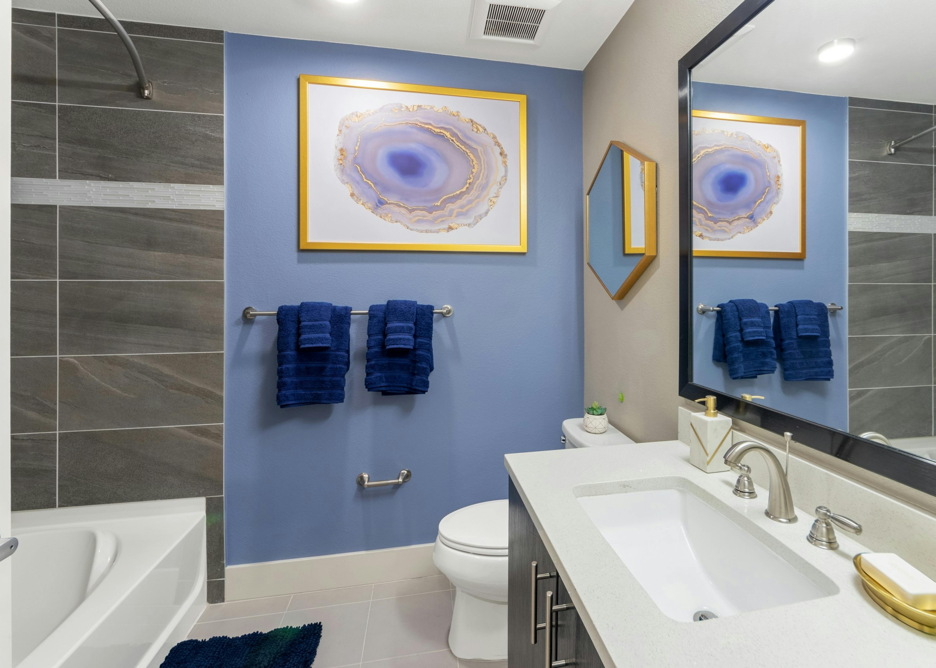 AMLI Riverfront Green apartment bathroom with periwinkle accent wall and gold accents with dark grey tiled shower tub