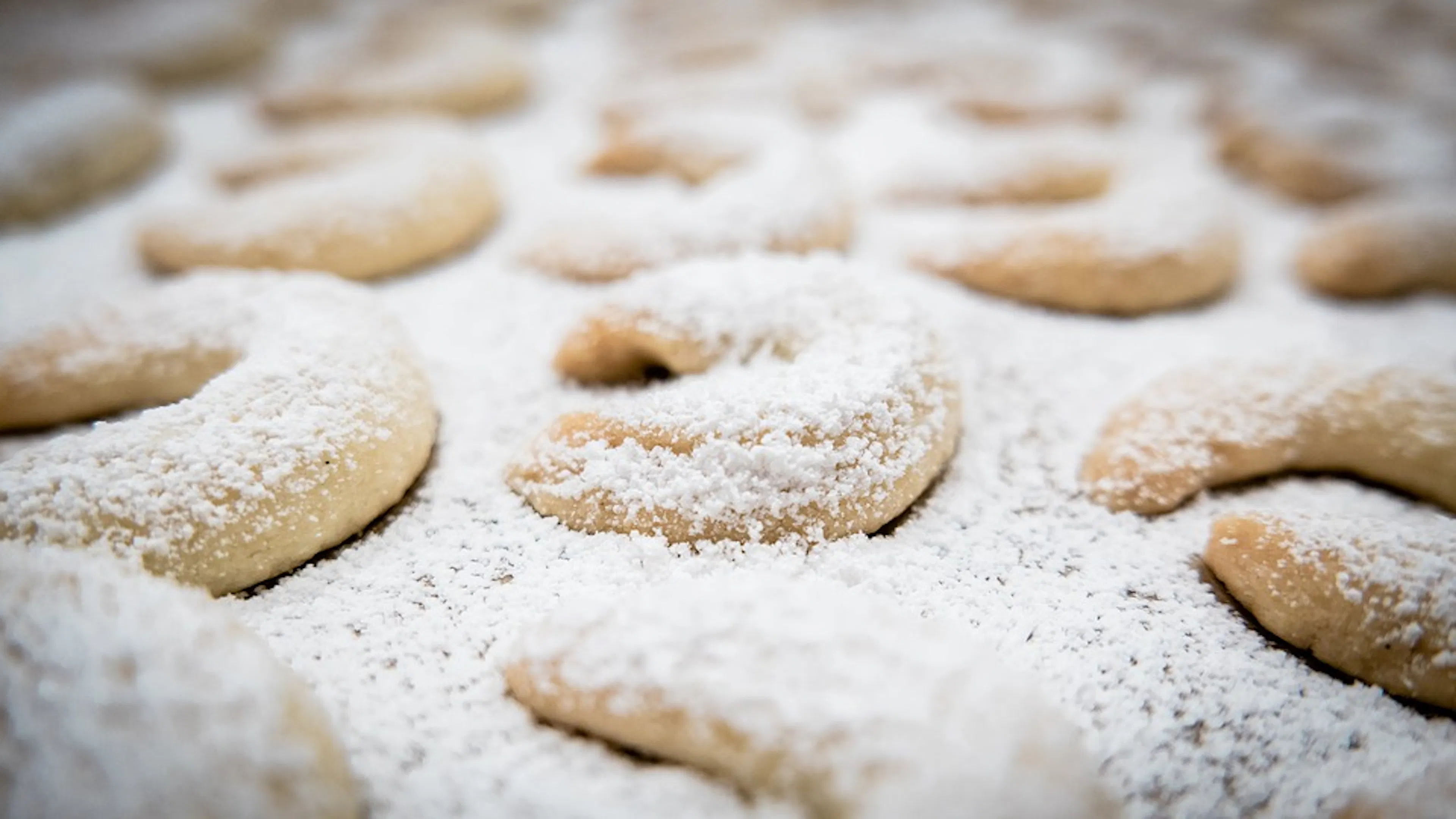 Close up of vanilla crescent cookies dusted in powdered sugar on a cookie tray