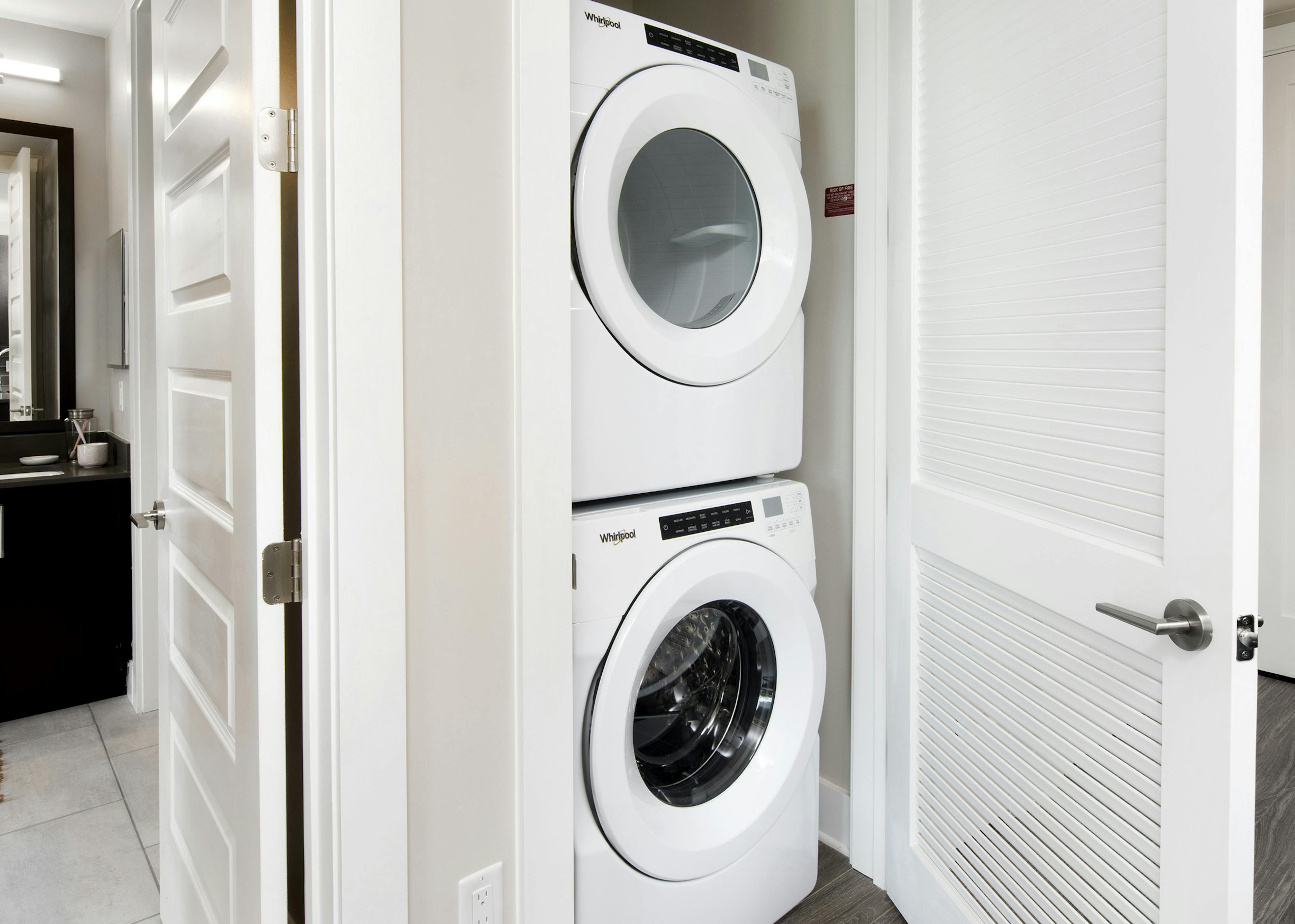 Interior view of AMLI Lenox apartment with white stackable washer and dryer in a closet with peak into bathroom at left