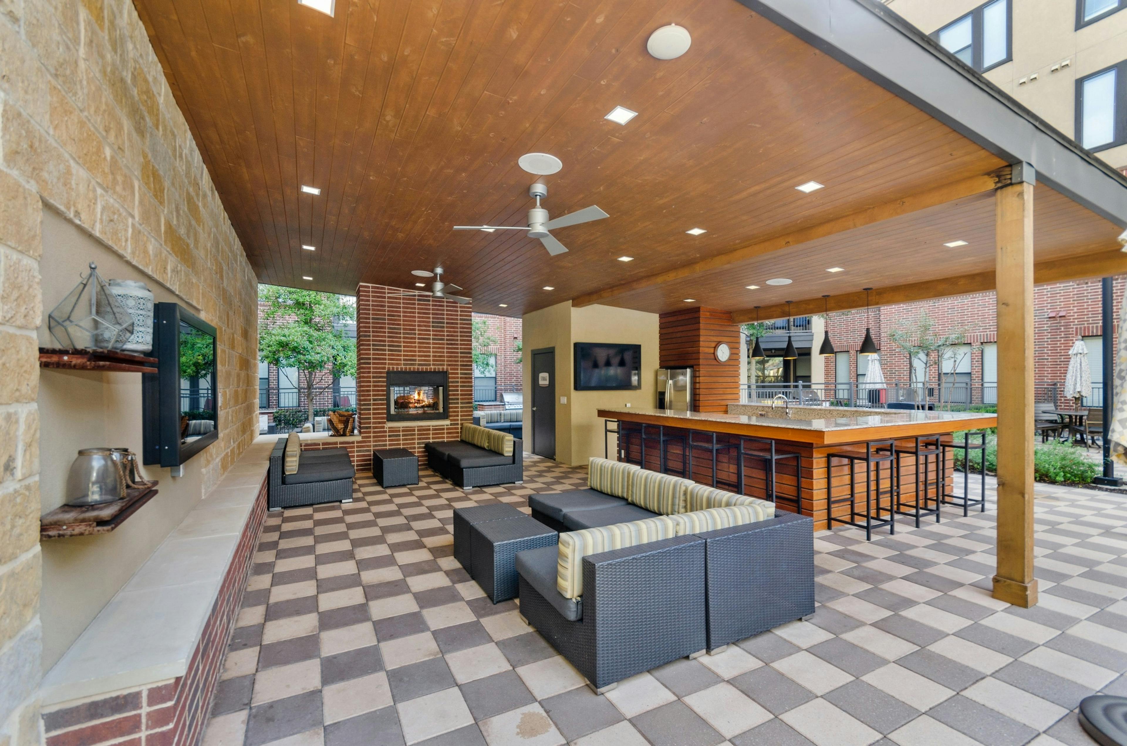 AMLI West Plano apartments outdoor covered kitchen surrounded by lounge and bar seating and next to an outdoor fireplace 