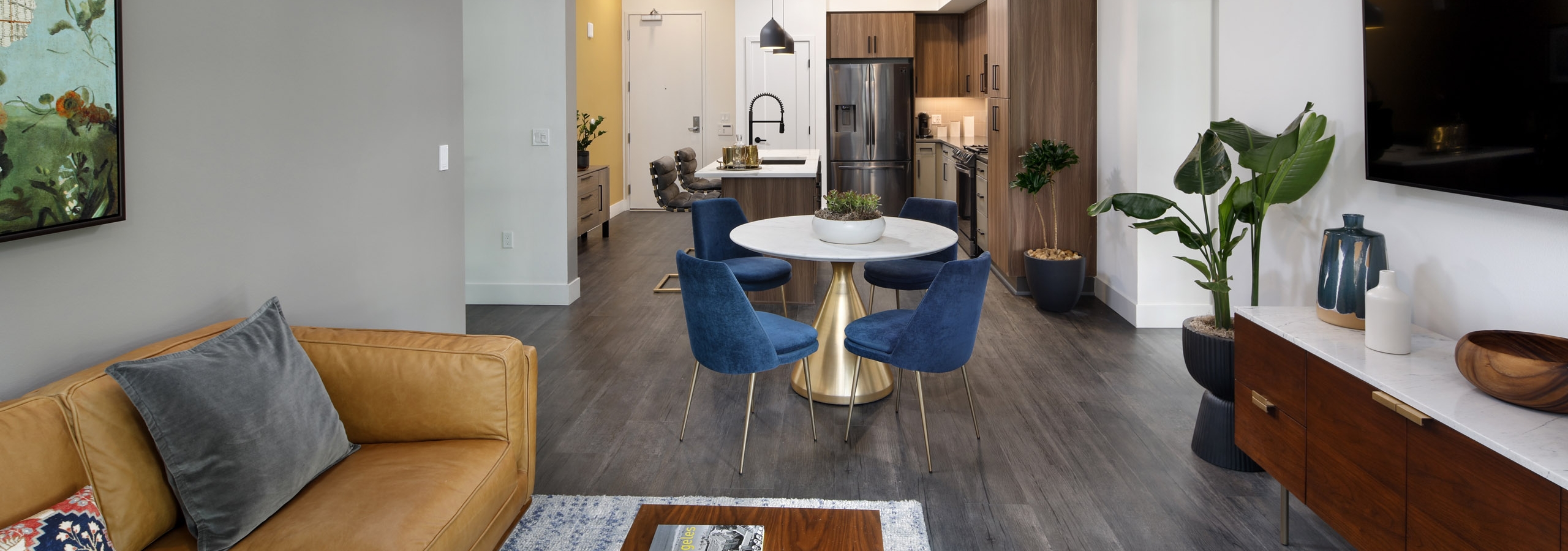 AMLI Old Pasadena living room with caramel leather sofa and dining table with blue chairs on gray floor and kitchen in rear