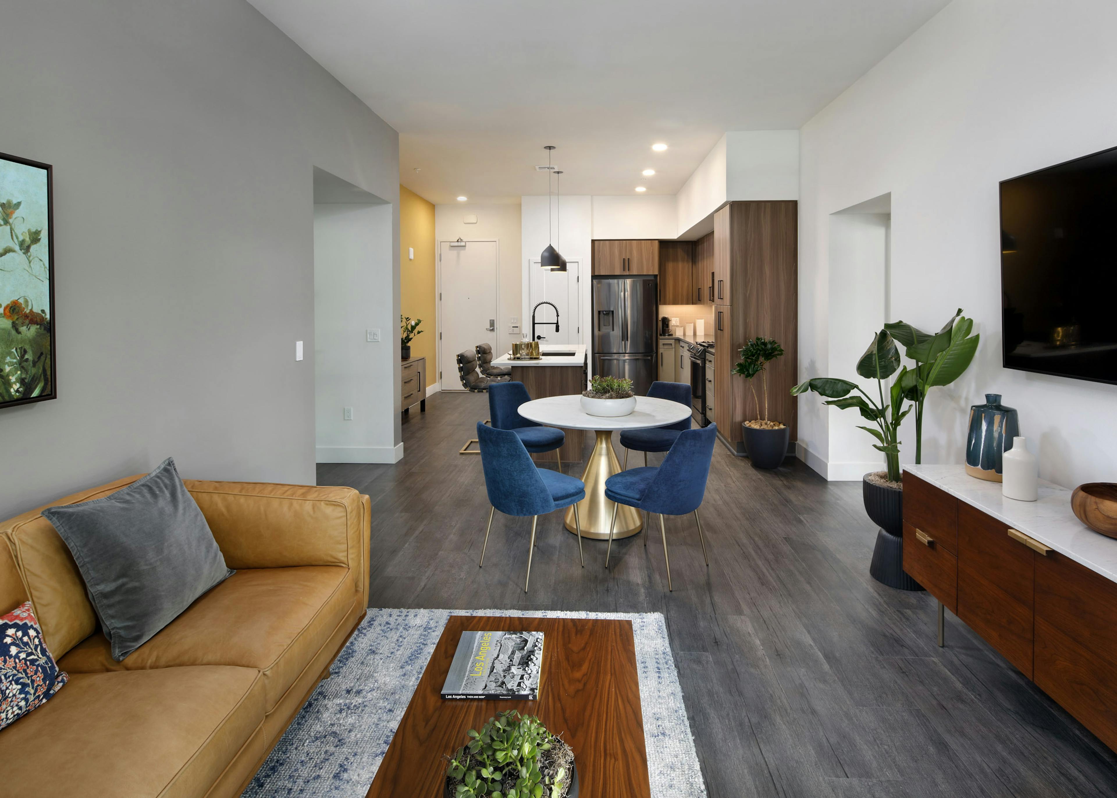 AMLI Old Pasadena living room with caramel leather sofa and dining table with blue chairs on gray floor and kitchen in rear