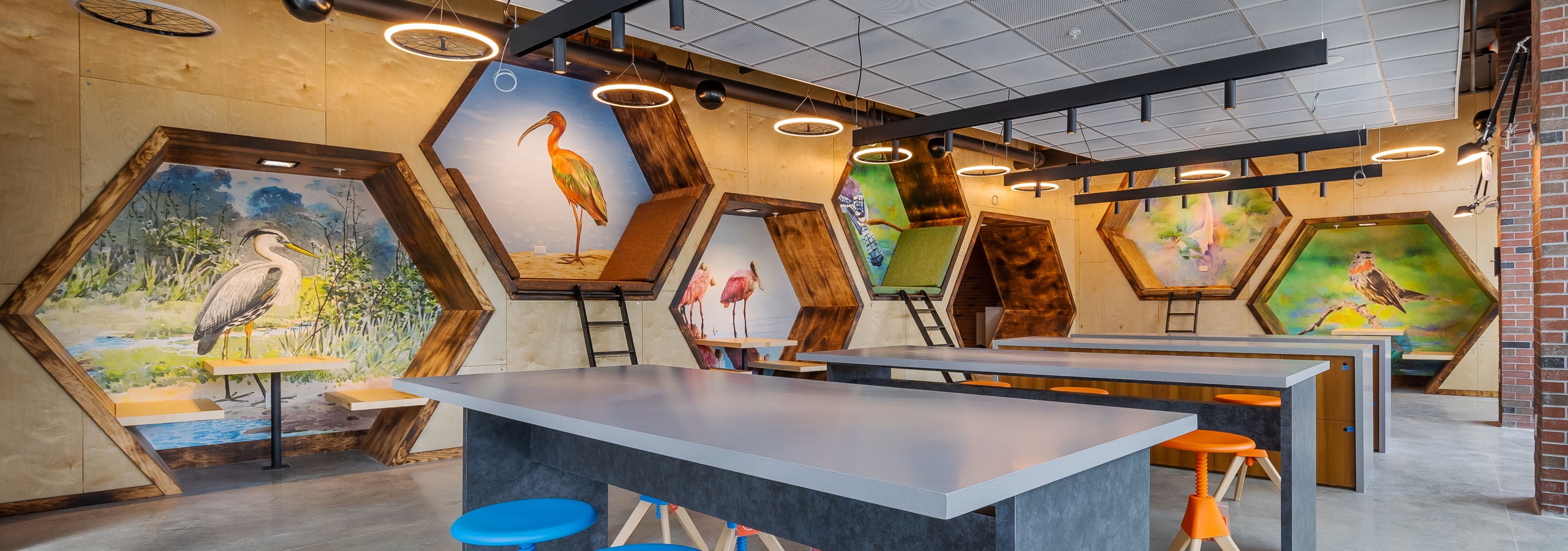 Interior view of AMLI Midtown Miami maker space with high top tables and stools with hexagon wall cutouts with bird art