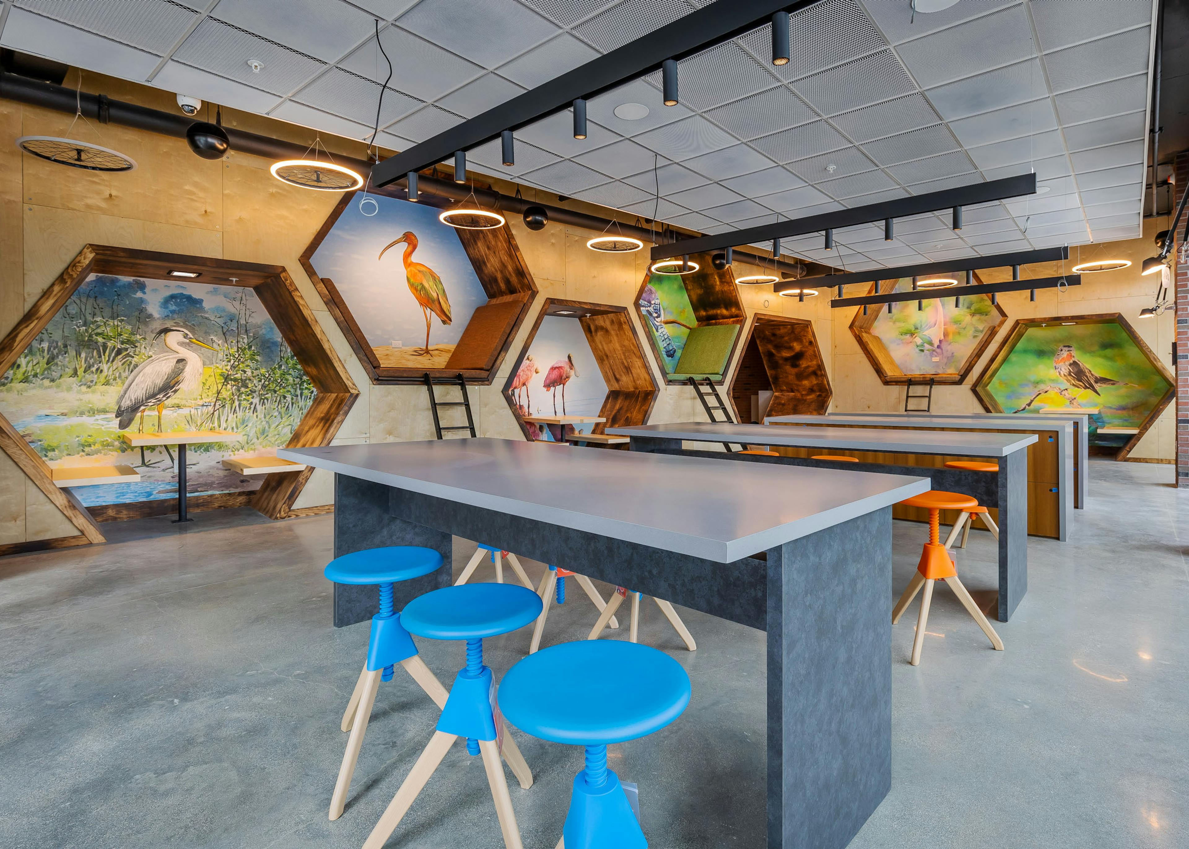 Interior view of AMLI Midtown Miami maker space with high top tables and stools with hexagon wall cutouts with bird art 