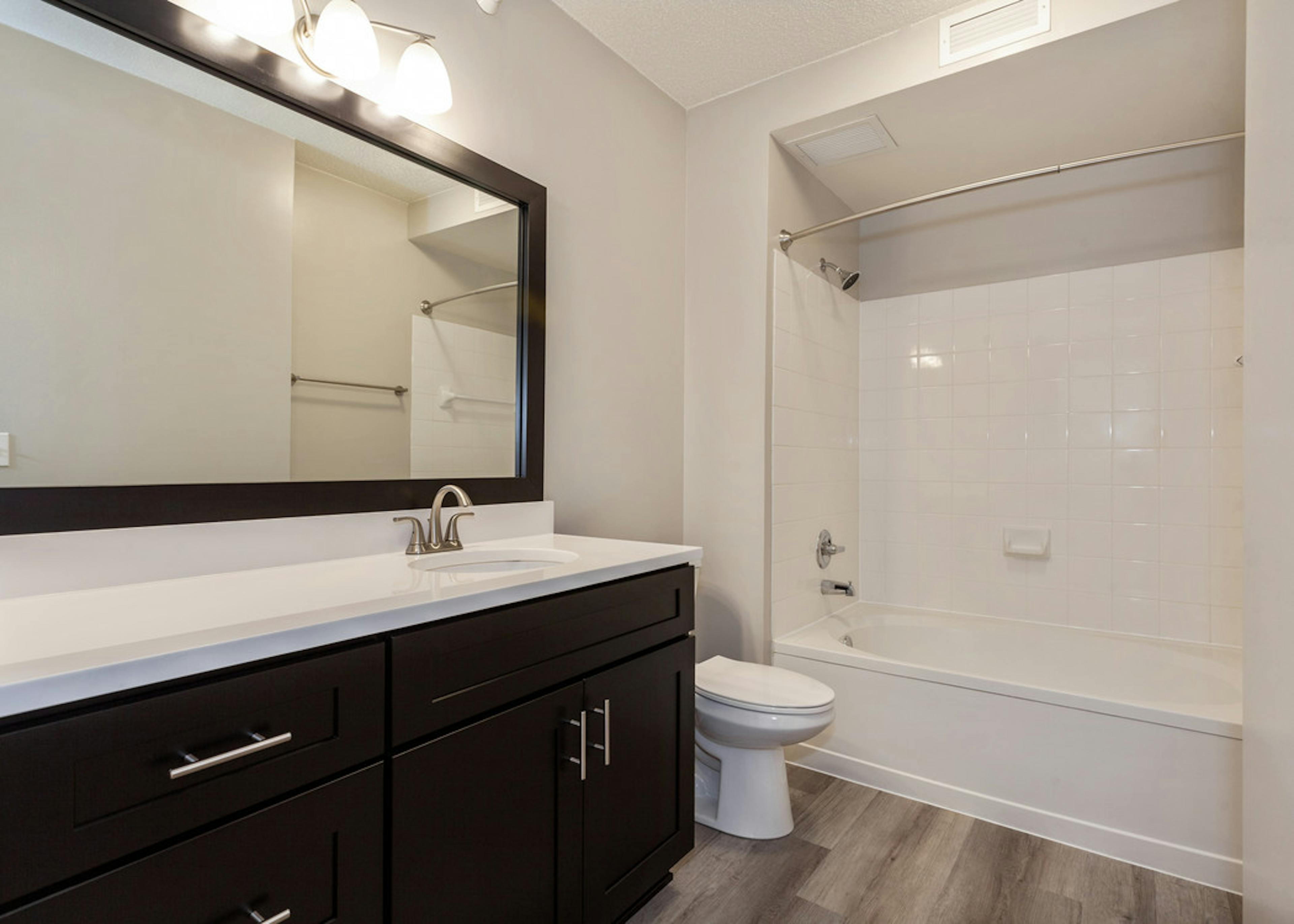 Interior of AMLI at Seven Bridges apartment bathroom with dark wood cabinets and white countertop and oval garden tub