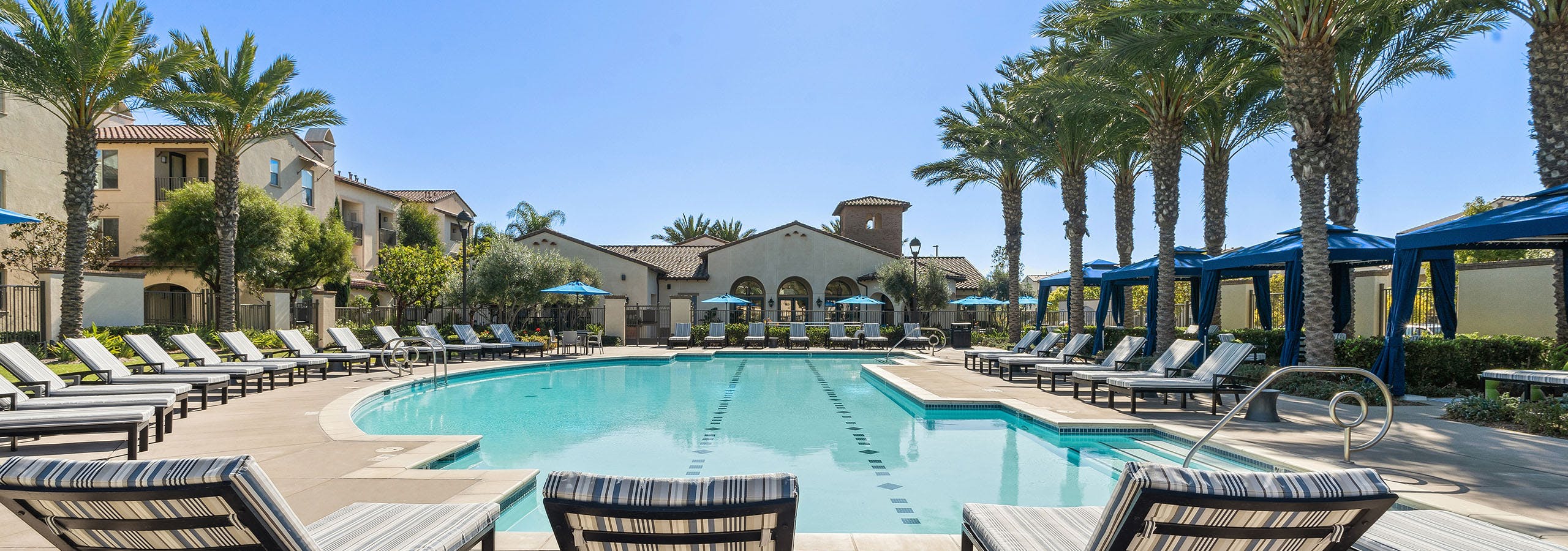 View of swimming pool surrounded by plentiful lounge seating and blue cabanas and tall palm trees at AMLI Spanish Hills