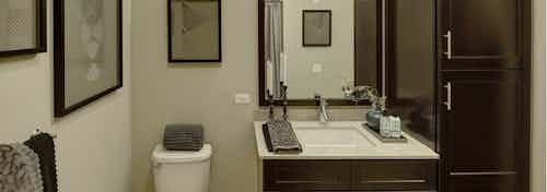 Interior view of a bathroom at AMLI River North with tan walls and a single dark wood vanity with a mirror next to a toilet