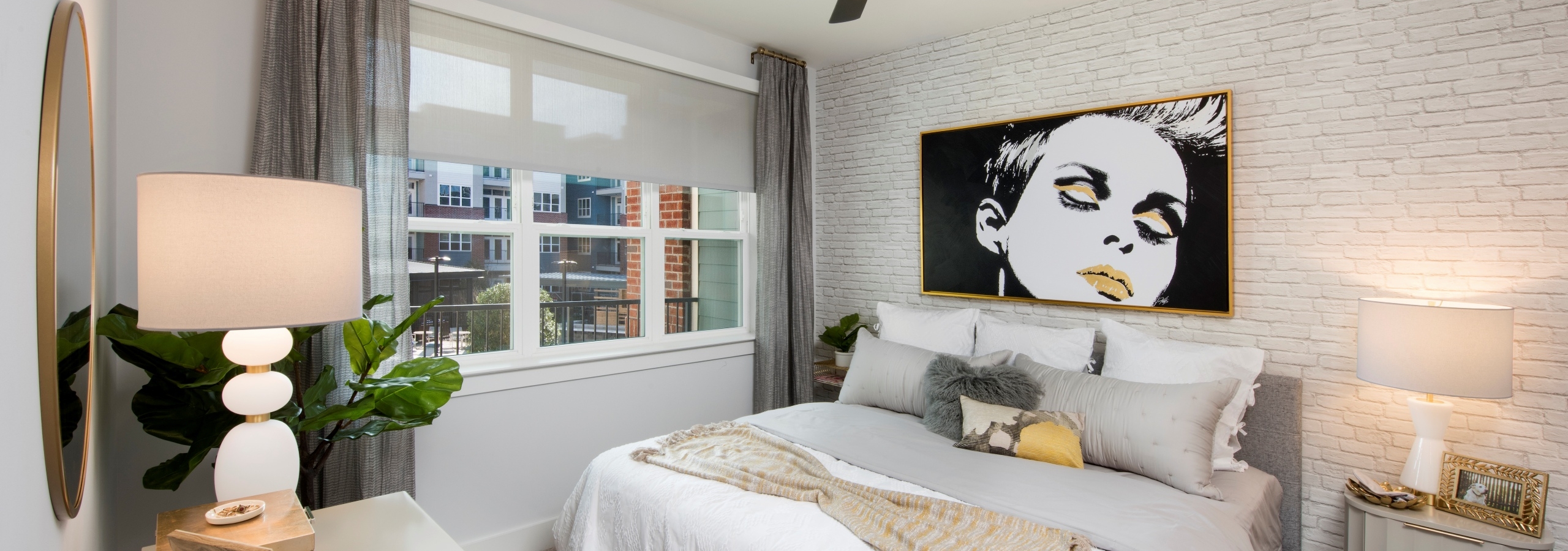 AMLI Decatur bedroom with bed centered on white brick wall with a retro art piece hanging above and with a window to the left