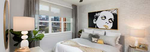 AMLI Decatur bedroom with bed centered on white brick wall with a retro art piece hanging above and with a window to the left