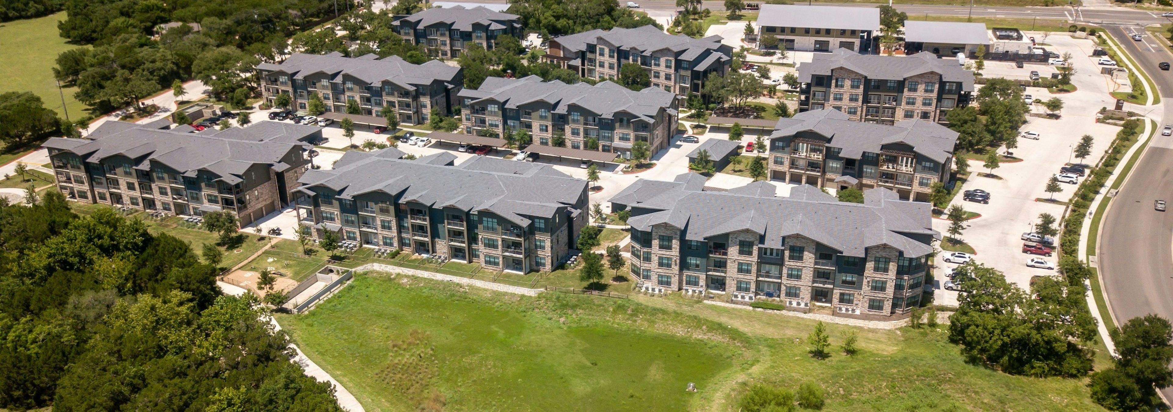 Daytime aerial view of AMLI Covered Bridge apartment community complex, surrounding green grass lawns, and parking