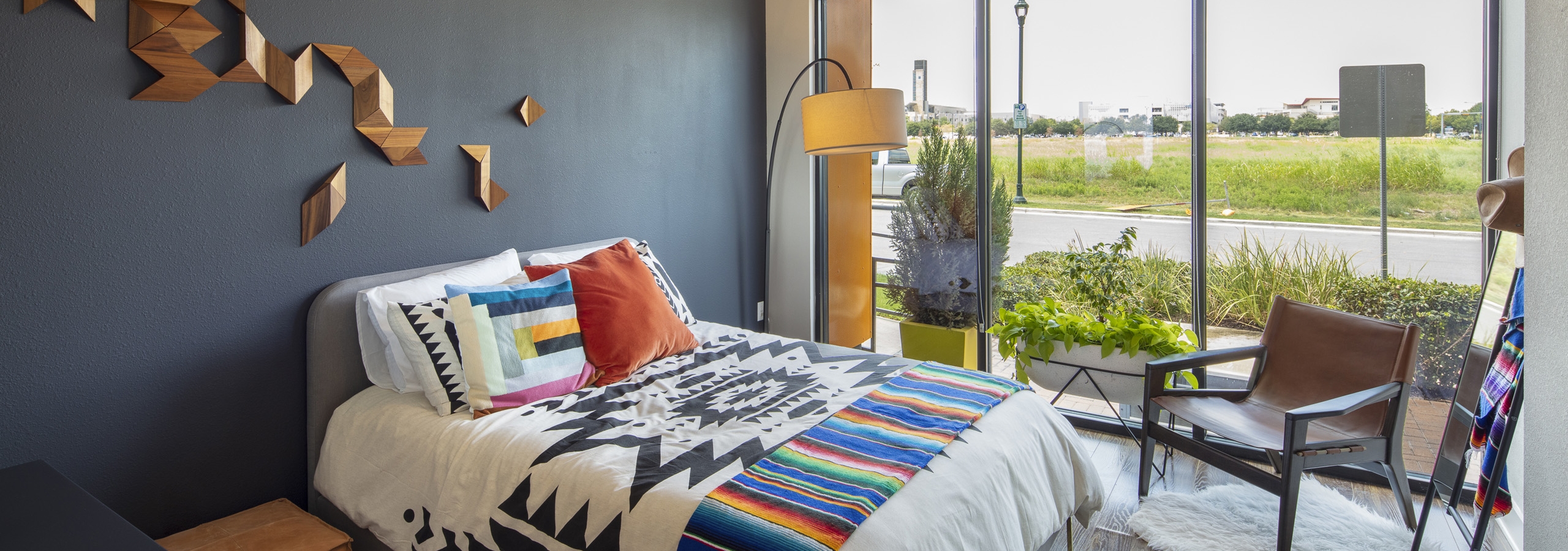 AMLI on Aldrich apartment bedroom with colorful bed on dark gray wall and floor to ceiling windows with view of green field