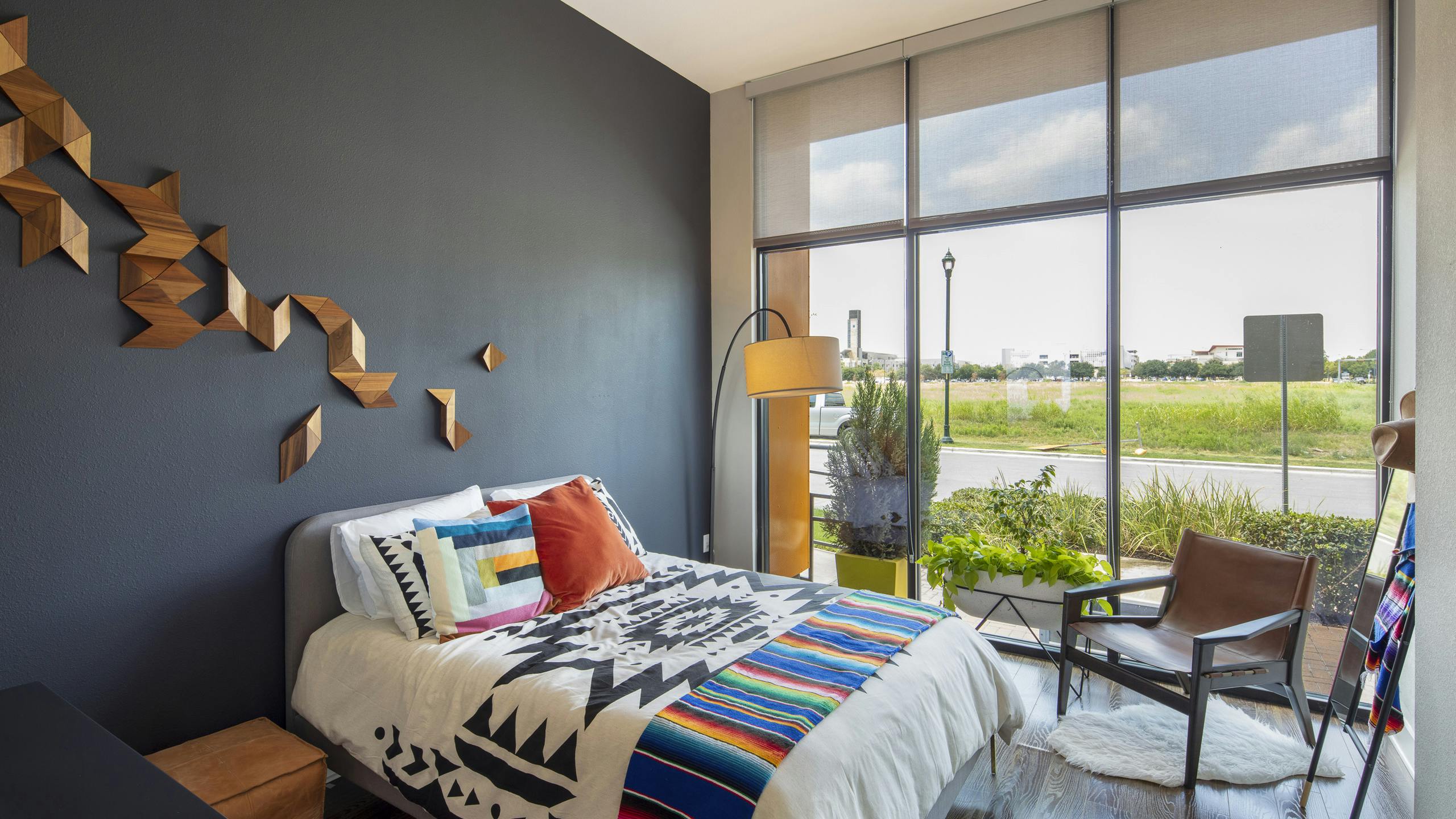 AMLI on Aldrich apartment bedroom with colorful bed on dark gray wall and floor to ceiling windows with view of green field