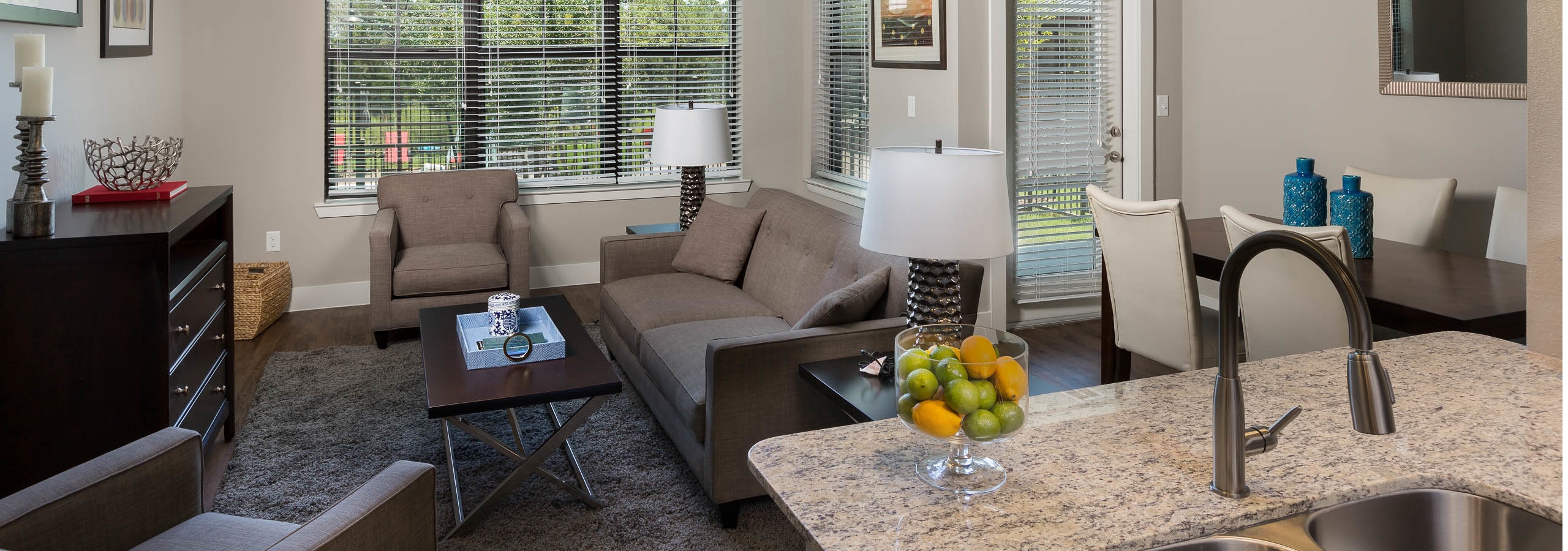 Interior of AMLI Covered Bridge living room and dining room with large windows with blinds, light walls and dark plank flooring