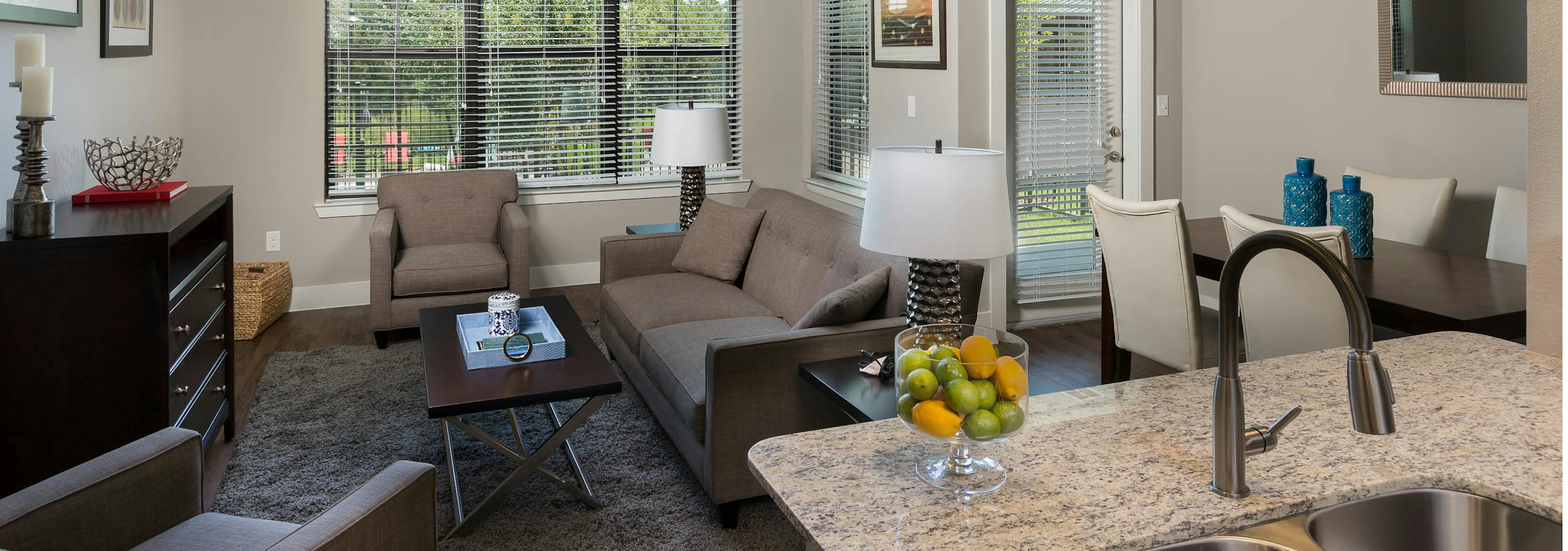 Interior of AMLI Covered Bridge living room and dining room with large windows with blinds, light walls and dark plank flooring