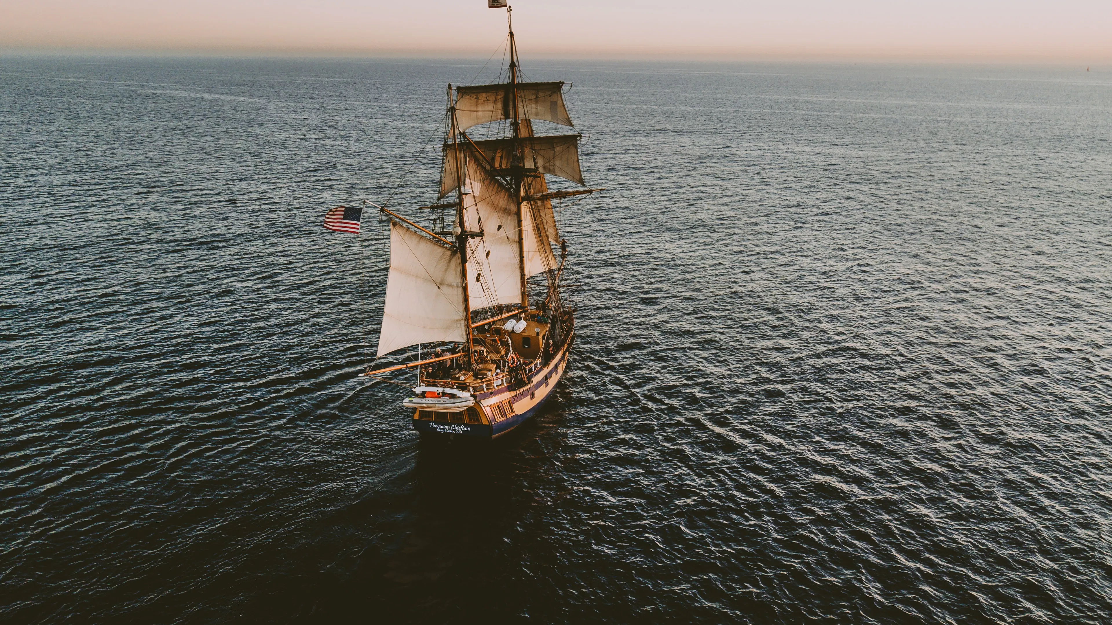 Three-masted pirate-style ship sailing the ocean flying an American flag.