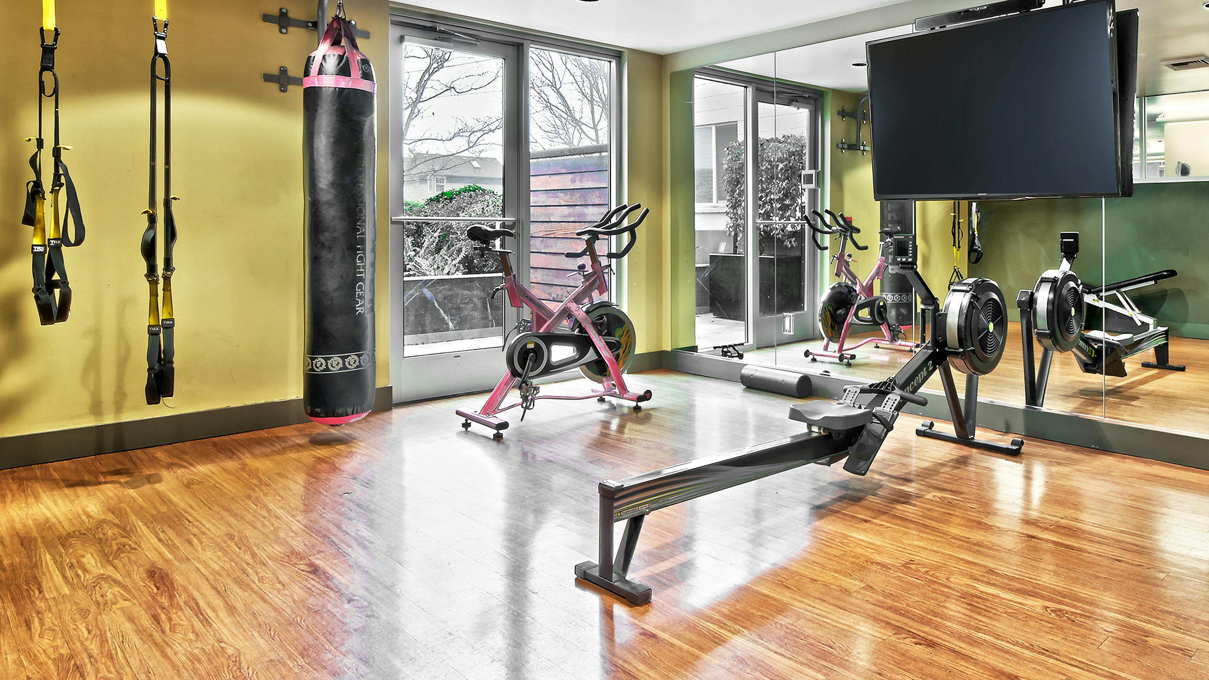 AMLI Mark24 yoga studio with yellow TRX straps and punching bag and spin bike and row maching and TV for fitness on demand