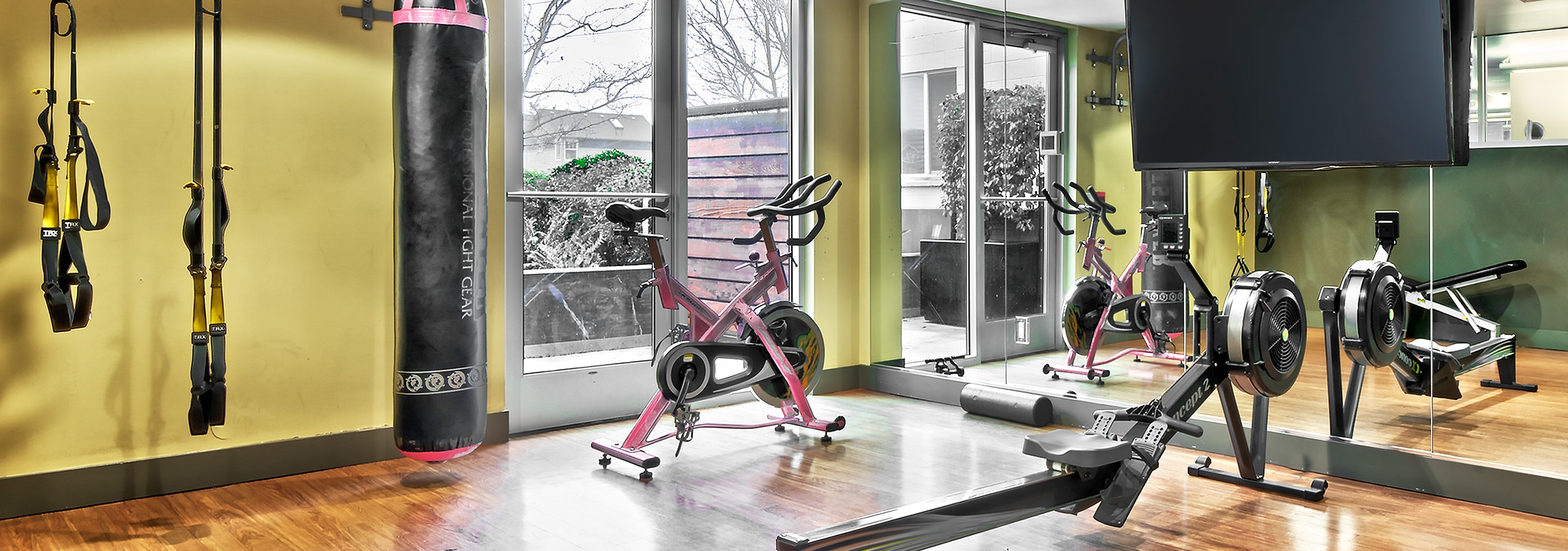 AMLI Mark24 yoga studio with yellow TRX straps and punching bag and spin bike and row maching and TV for fitness on demand