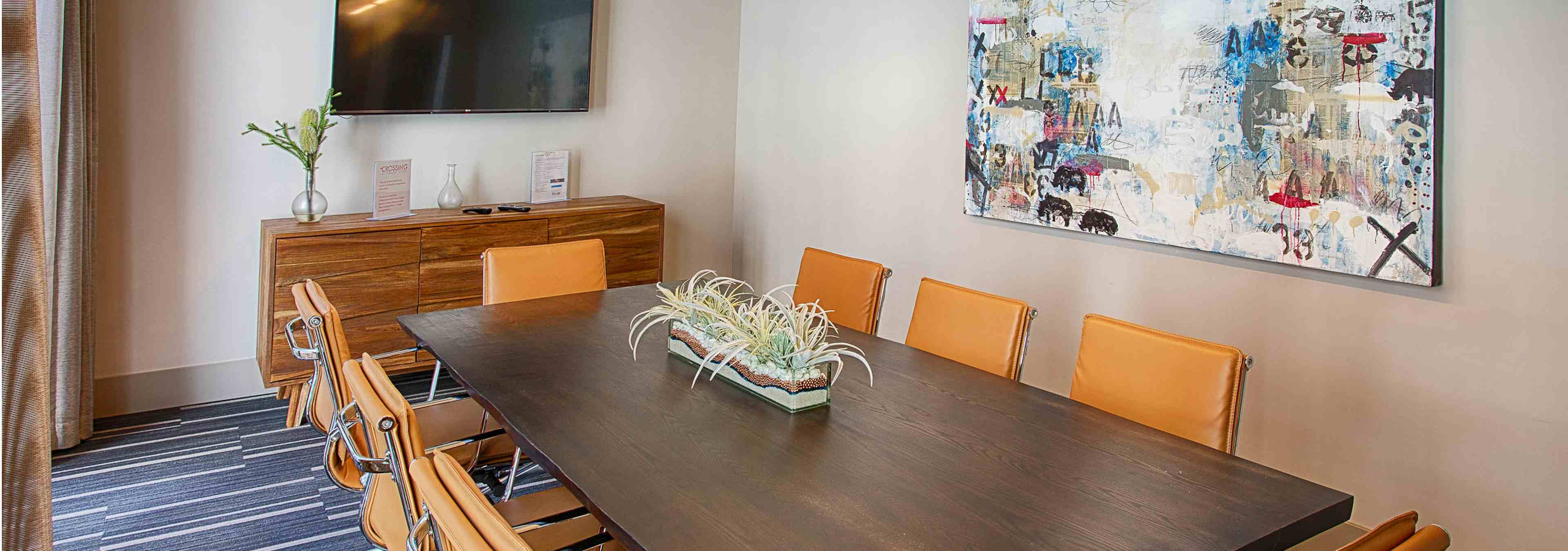 A conference room at AMLI Denargo Market apartments with a long table and chairs and a large piece of art and television 