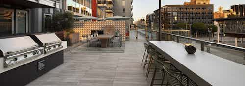 Dusk view of AMLI Park Broadway apartment building rooftop lounge with two long tables and chairs and two barbecue grills