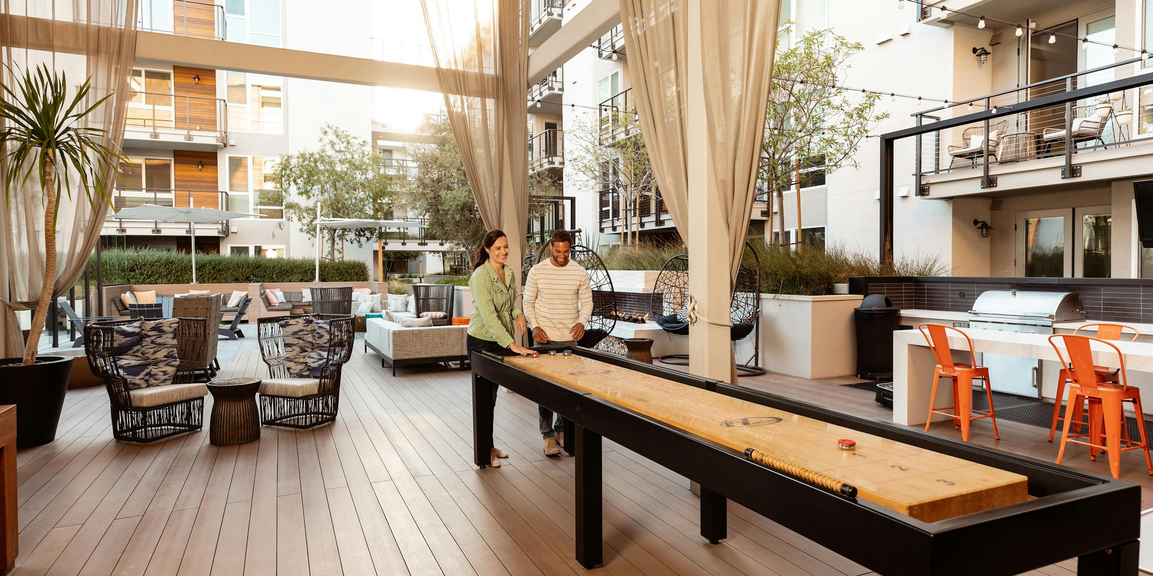 AMLI Marina Del Rey apartment residents playing shuffleboard with luxurious lounge chairs and white modern building exterior