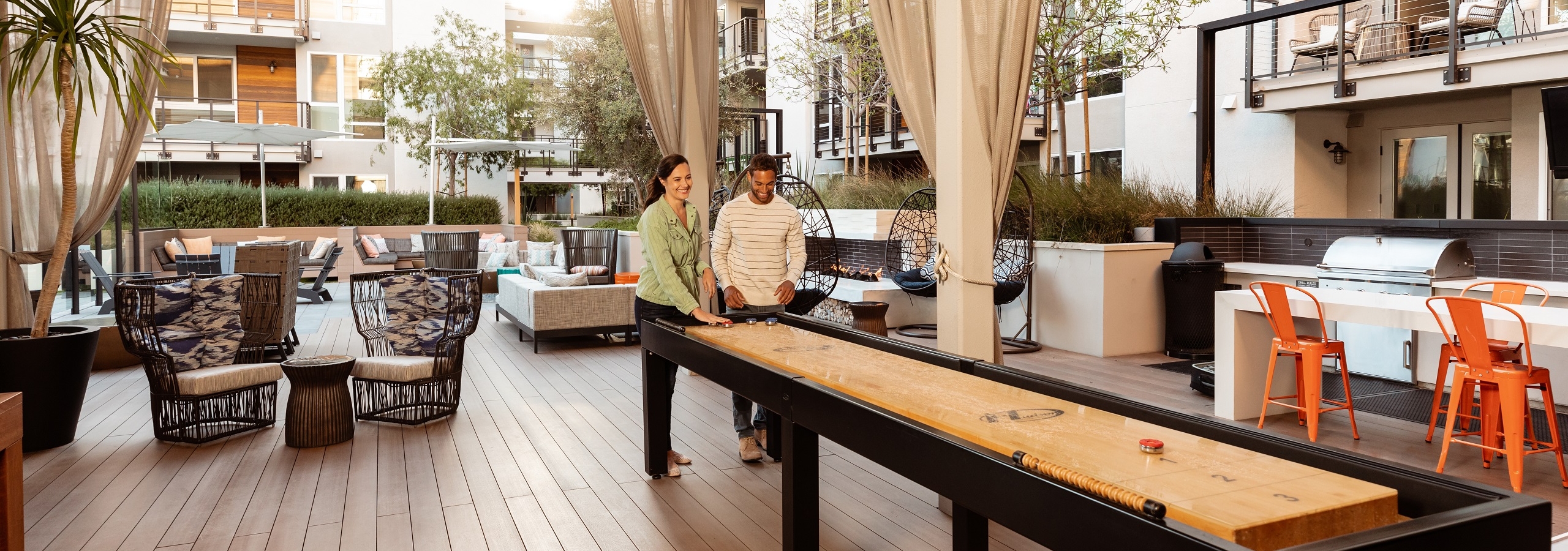 AMLI Marina Del Rey apartment residents playing shuffleboard with luxurious lounge chairs and white modern building exterior