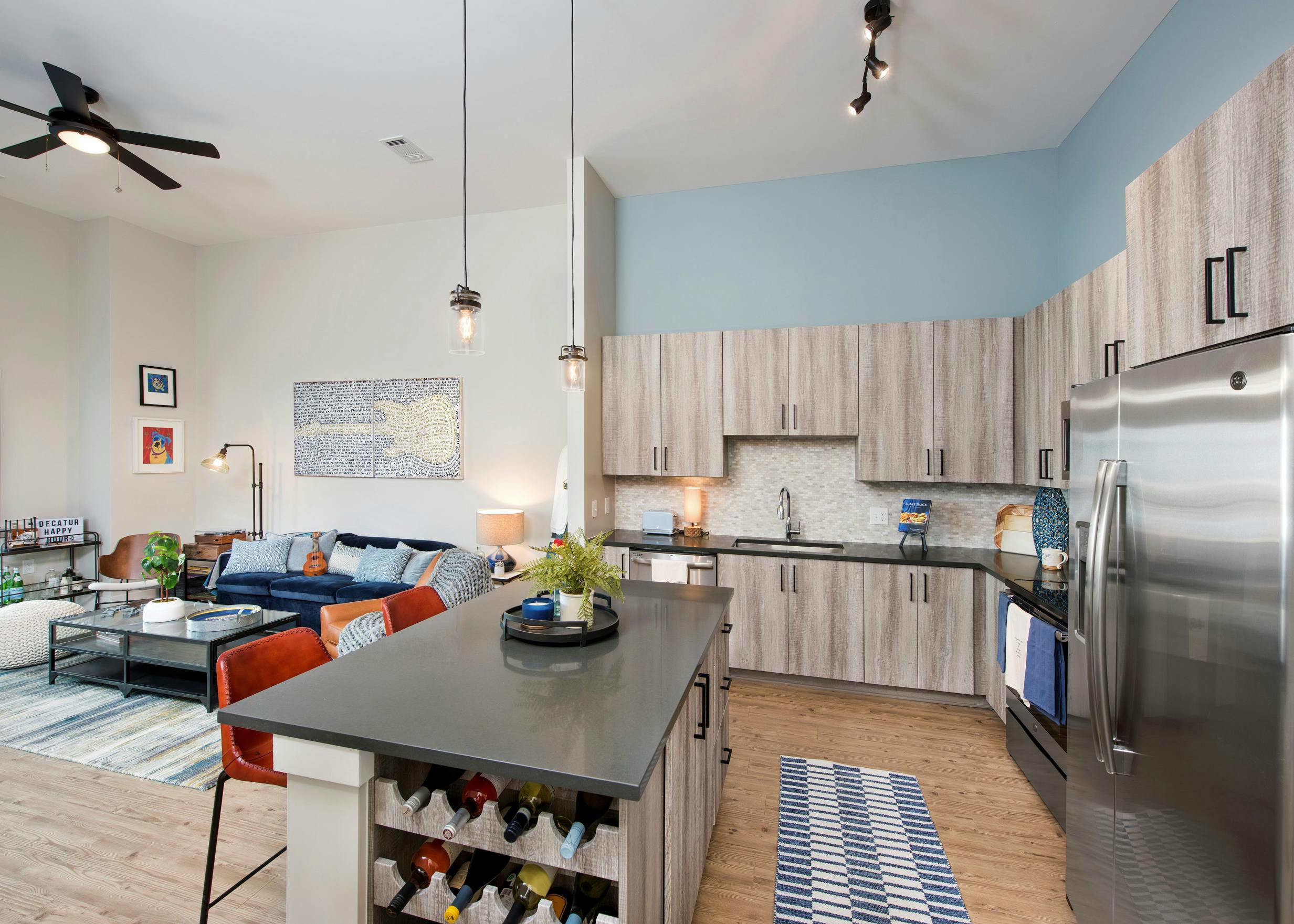 Interior view of AMLI Dectaur apartment kitchen with quartz countertops and stainless steel appliances and living room