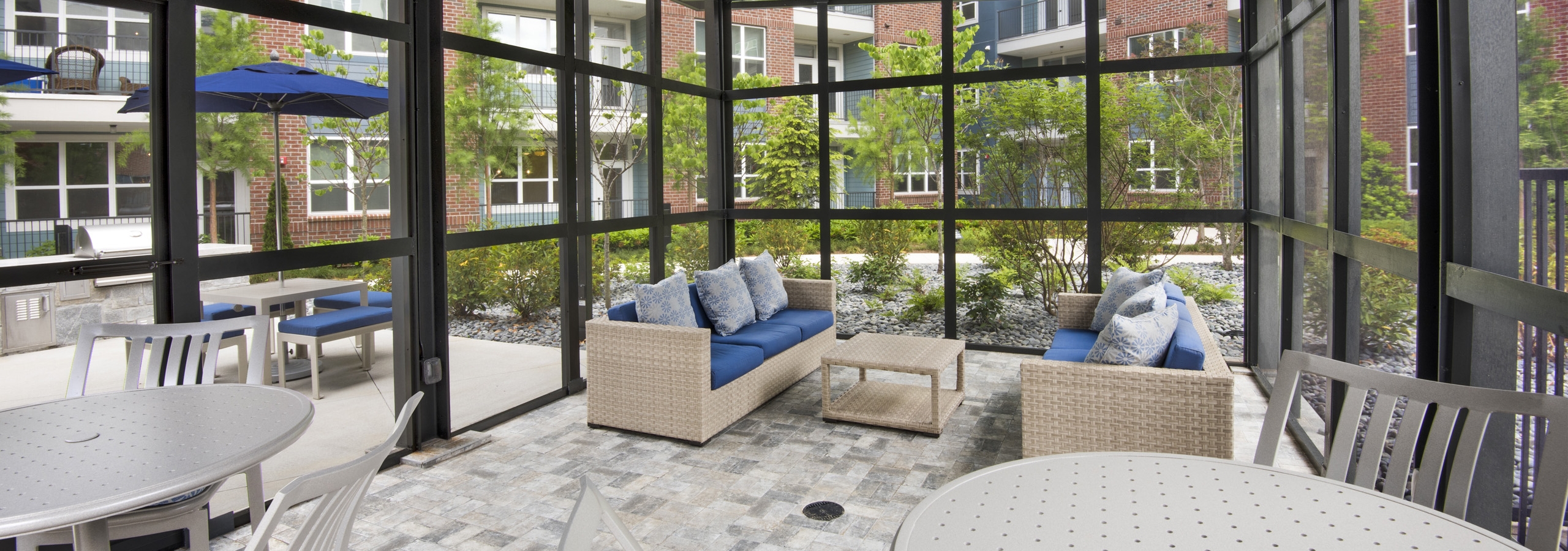Interior view of the screened pool cabana at AMLI Decatur on a sunny day with sofa and blue pillows and white tables