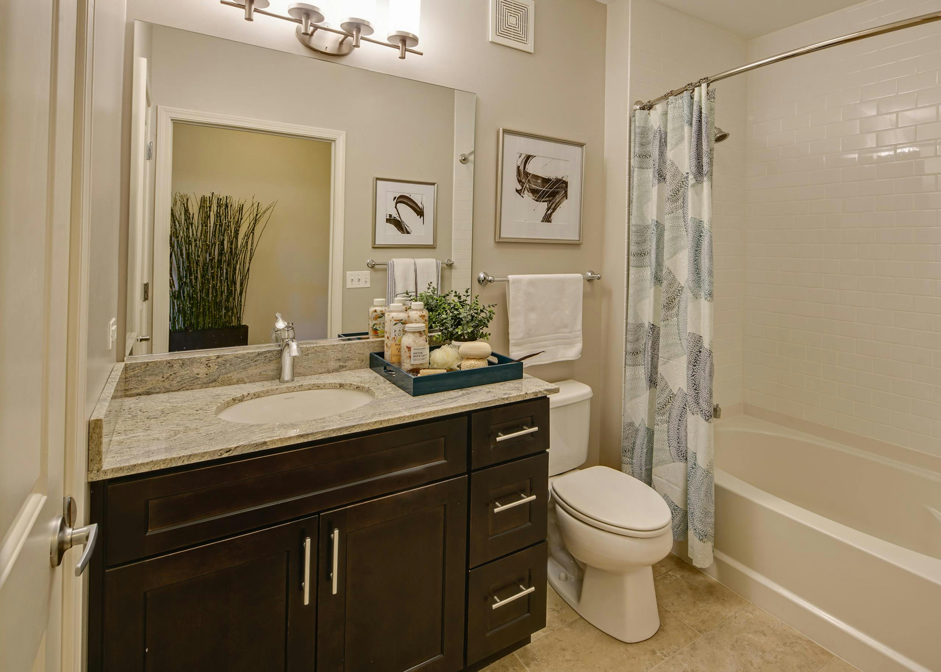 AMLI Evanston apartment bathroom featuring a subway tiled shower and a granite vanity sink with dark cabinetry