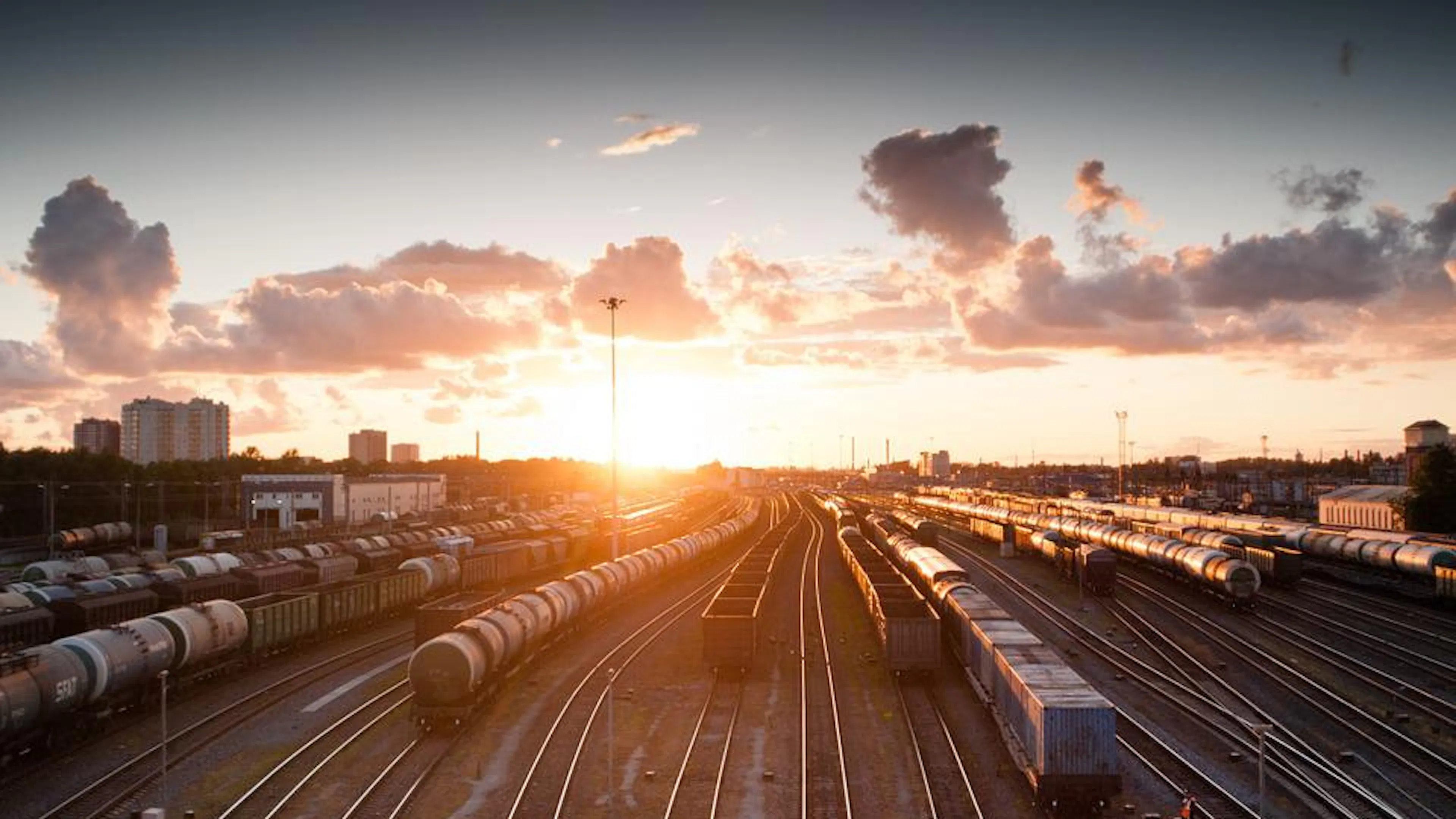 A train track yard with some trains parked on them and the sun setting behind them