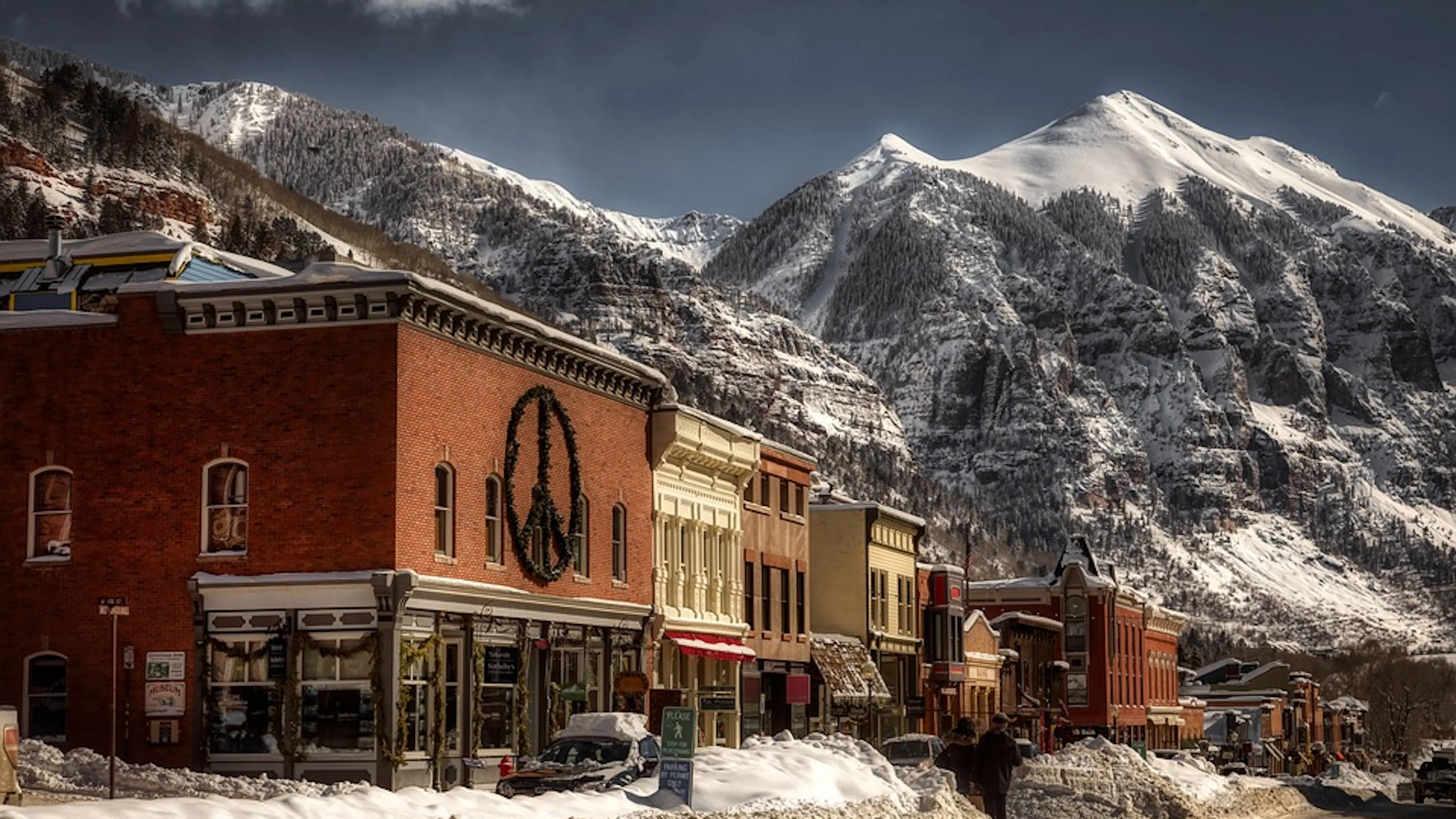 A street of a historic downtown buildings covered with snow with a huge snowy peak towering in the background