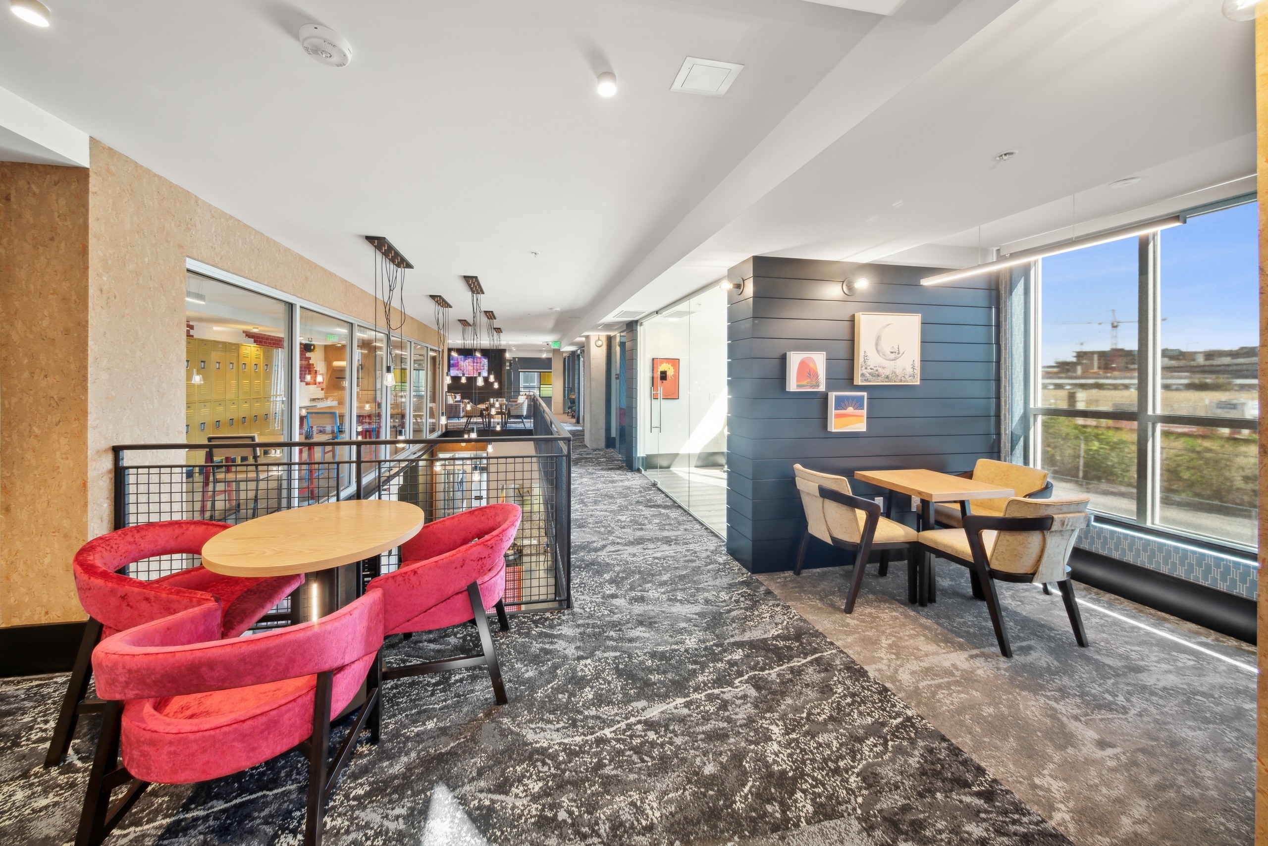 AMLI RiNo 2 story coworking space with wood tables and chairs on gray patterned carpet and window with view to outdoors
