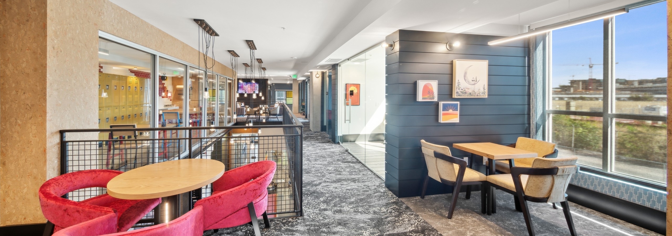 AMLI RiNo 2 story coworking space with wood tables and chairs on gray patterned carpet and window with view to outdoors