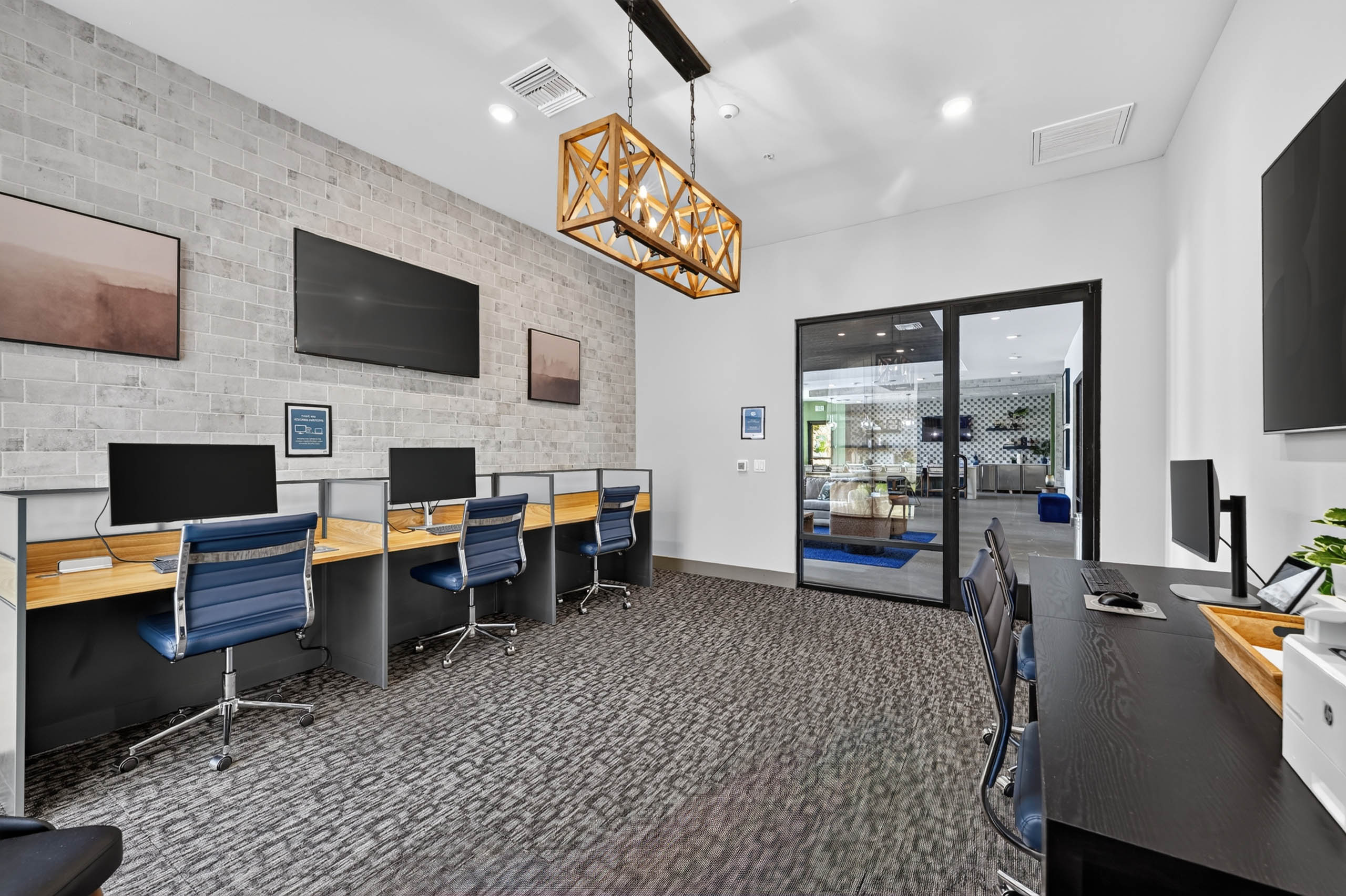 Business center at AMLI Camarillo apartments with computer workstations, blue office chairs, televisions and glass doors.