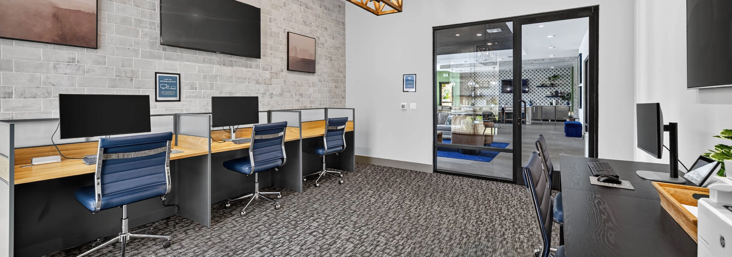 Business center at AMLI Camarillo apartments with computer workstations, blue office chairs, televisions and glass doors.