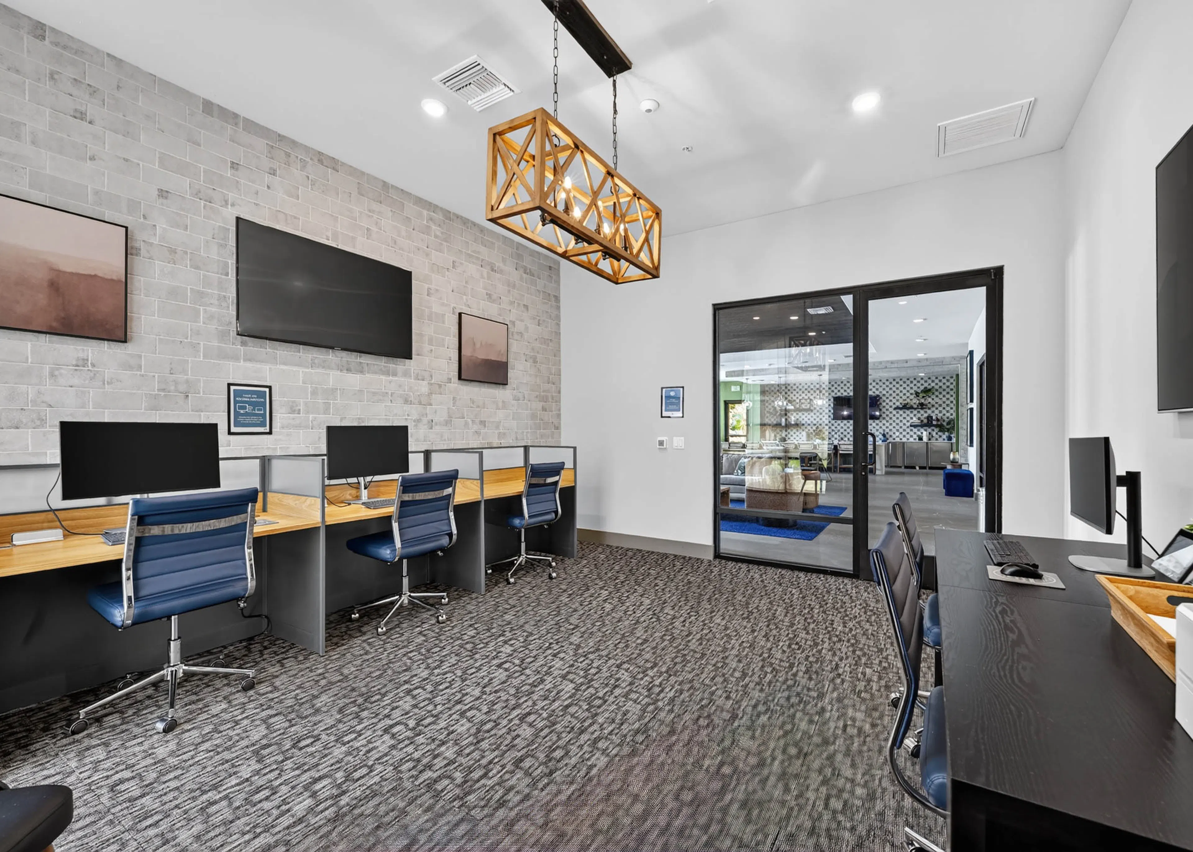 Business center at AMLI Camarillo apartments with computer workstations, blue office chairs, televisions and glass doors.