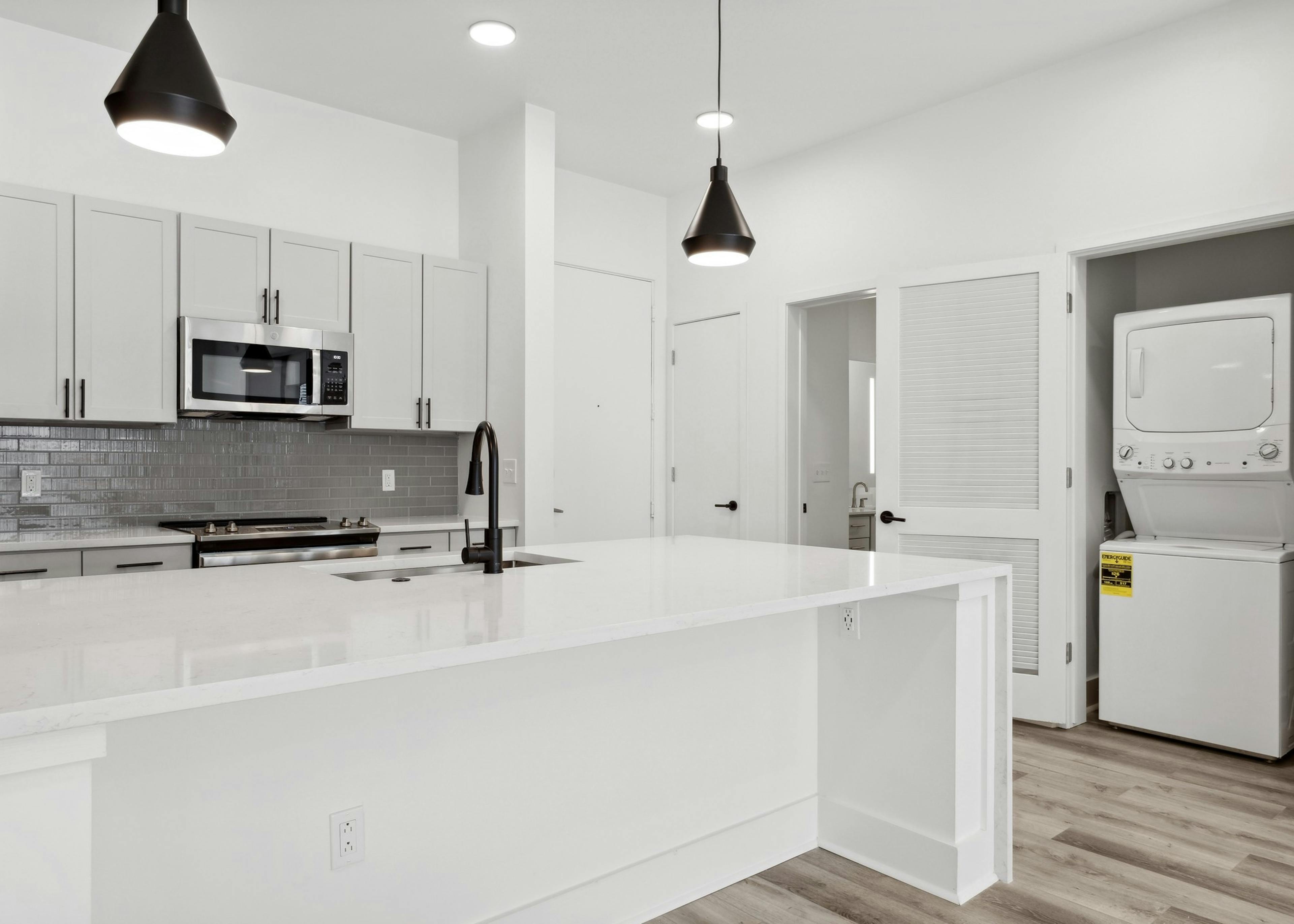 Island kitchen with white counter tops and cabinets and gray tiled backsplash with view of laundry closet at AMLI Old 4th Ward